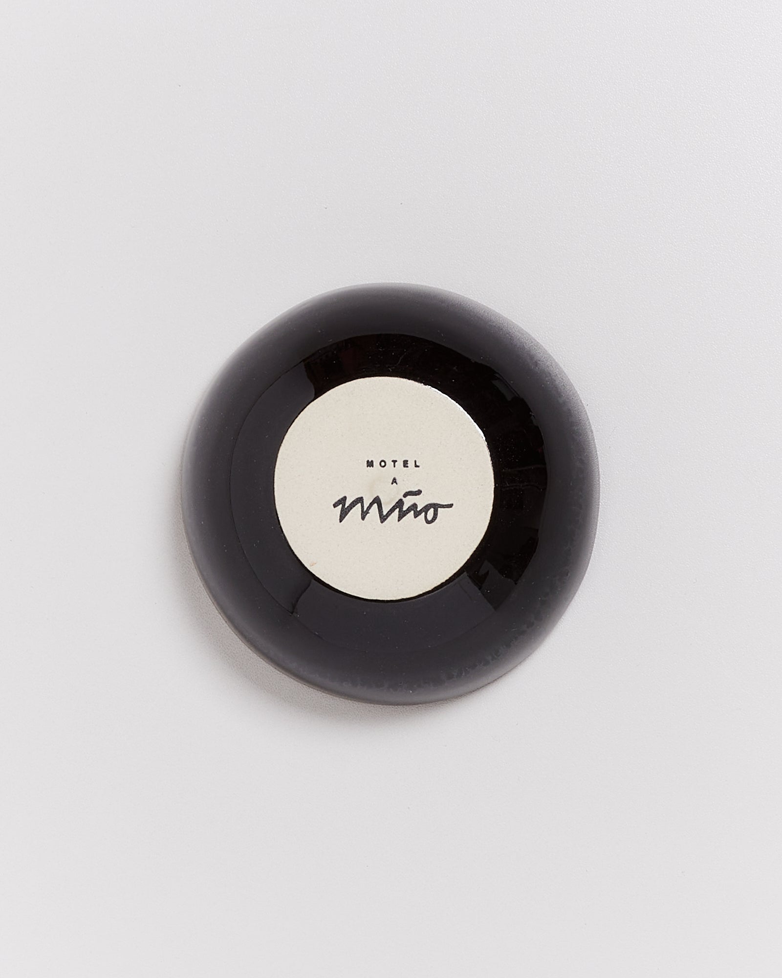 Runde schwarze Schale mit beigem Inneren und der Aufschrift "Motel a mio" auf heller Oberfläche.