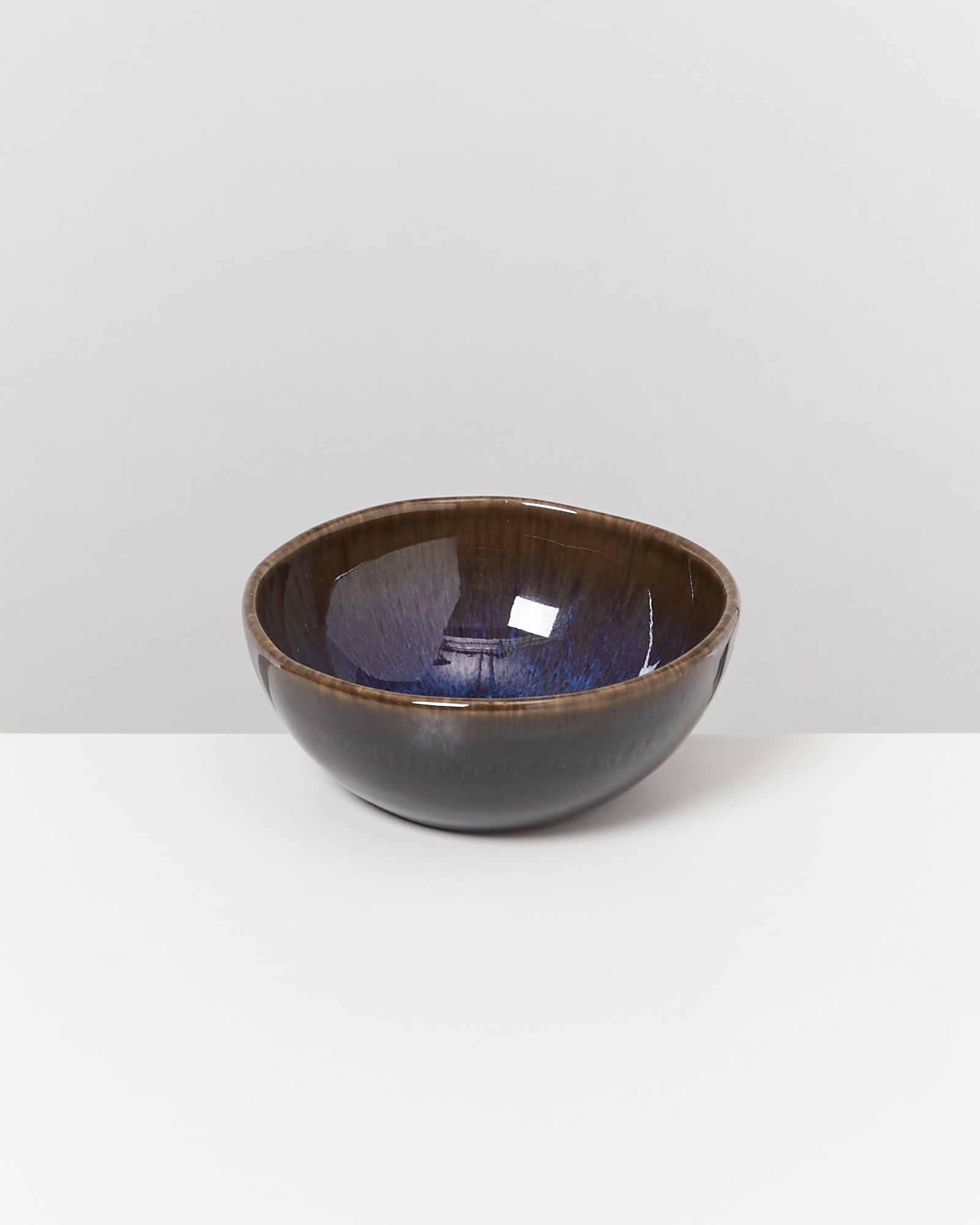 Braune Keramikschale mit bläulichem Innenmuster auf weißem Hintergrund.