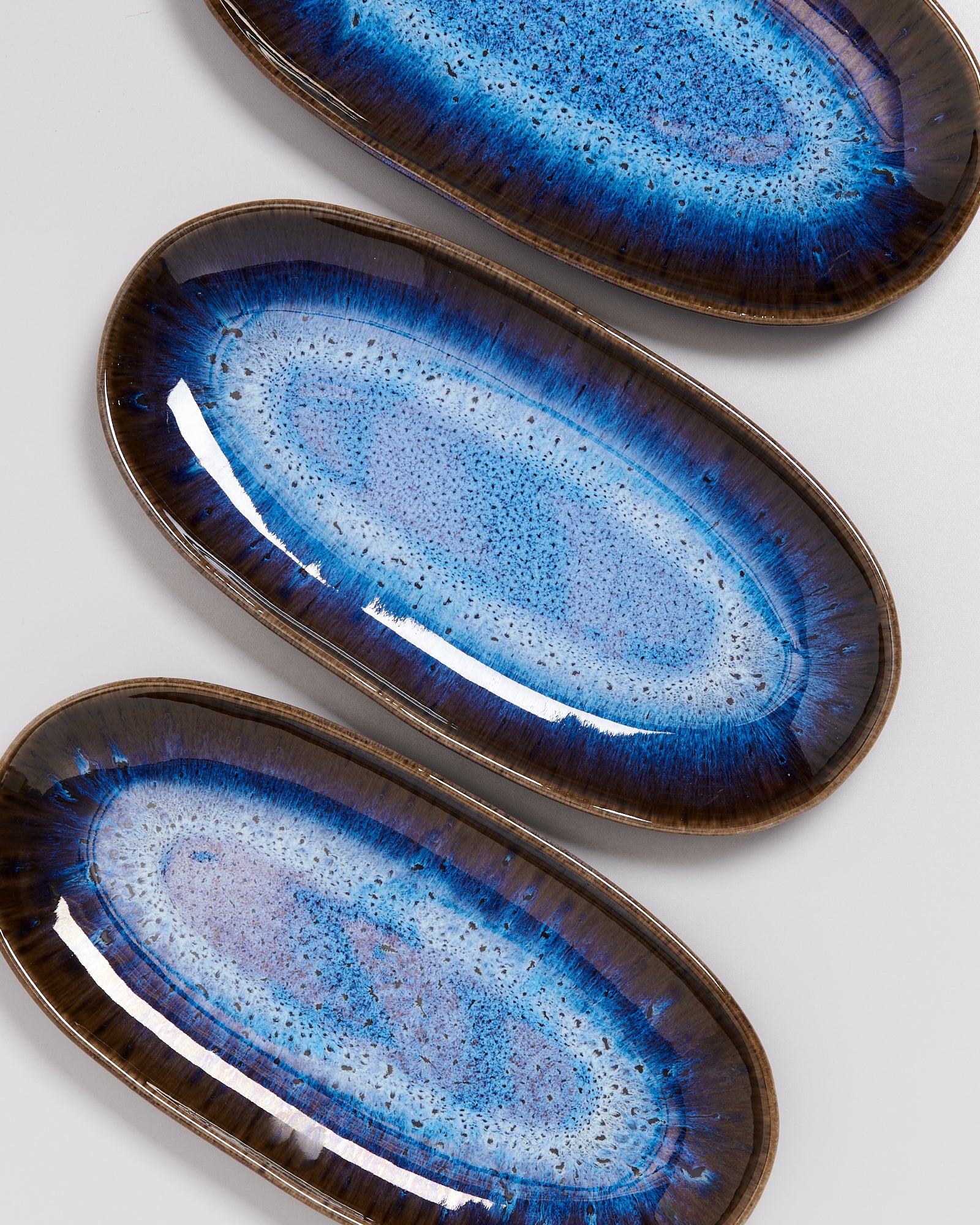 Drei ovale Keramikteller mit blauem und braunem Muster auf grauem Hintergrund.
