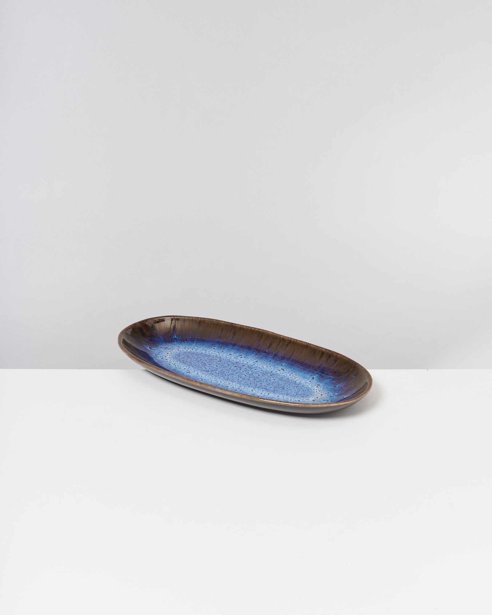 Länglicher, brauner Keramikteller mit blauer Glasur auf weißem Hintergrund.