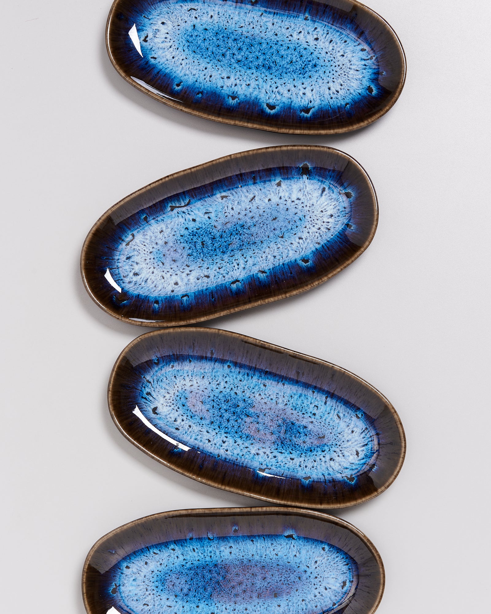 Vier ovale Keramikteller mit blauem, gesprenkeltem Muster und dunklem Rand auf weißem Hintergrund.