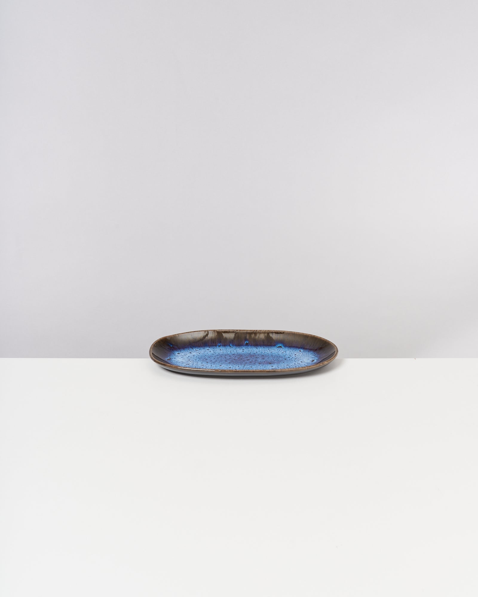 Ovaler Keramikteller mit blauer Glasur auf einem weißen Hintergrund.