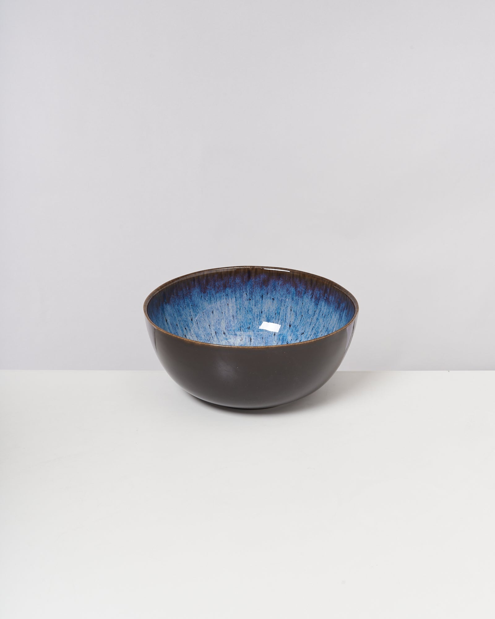 Keramikschüssel mit blauem Innenbereich und dunklem Äußeren steht auf weißer Oberfläche.