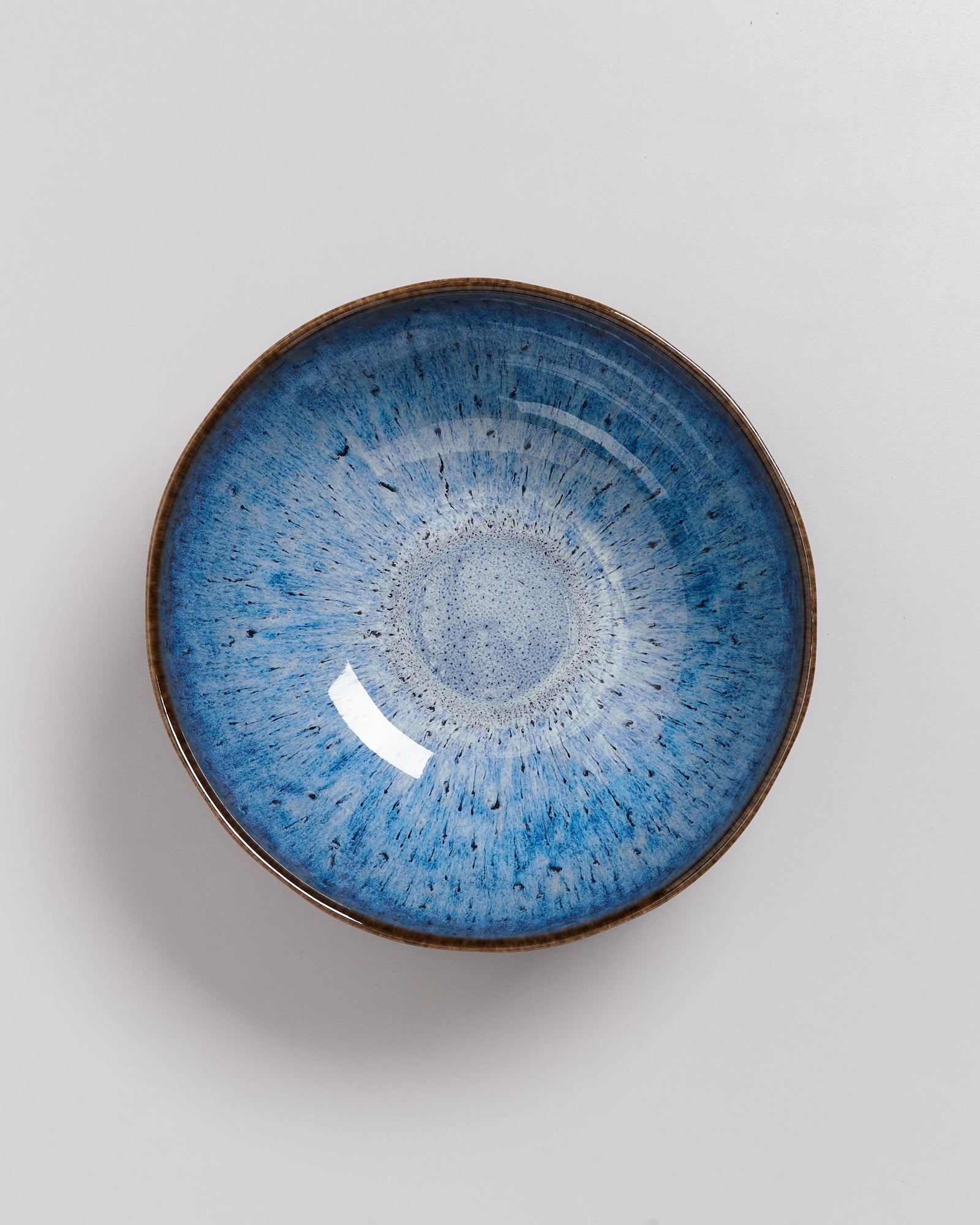 Blaue Keramikschüssel mit braunem Rand und gesprenkeltem Muster auf hellem Hintergrund.