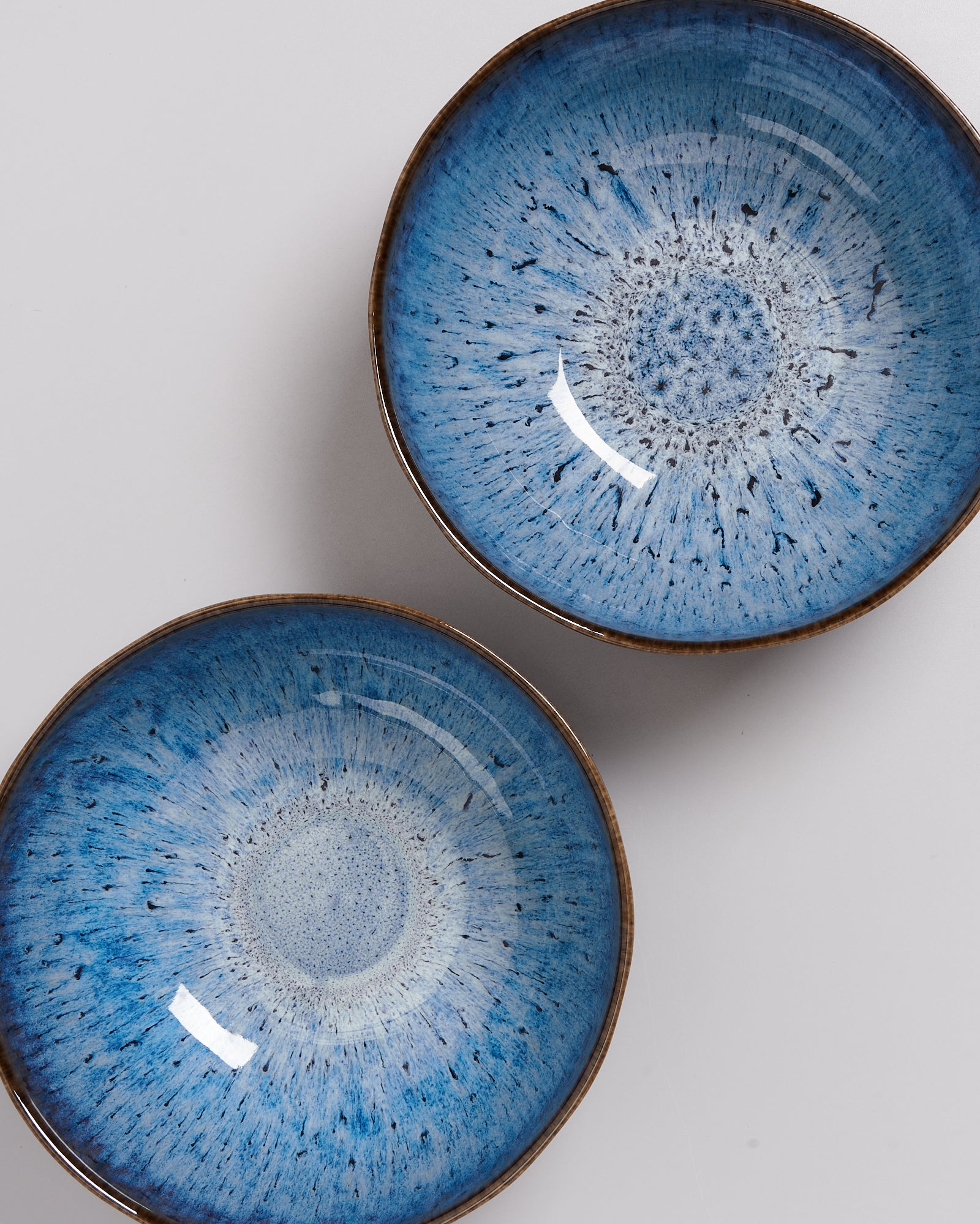 Zwei blaue Keramikschalen mit spiralförmigem Muster, auf einer weißen Oberfläche liegend.