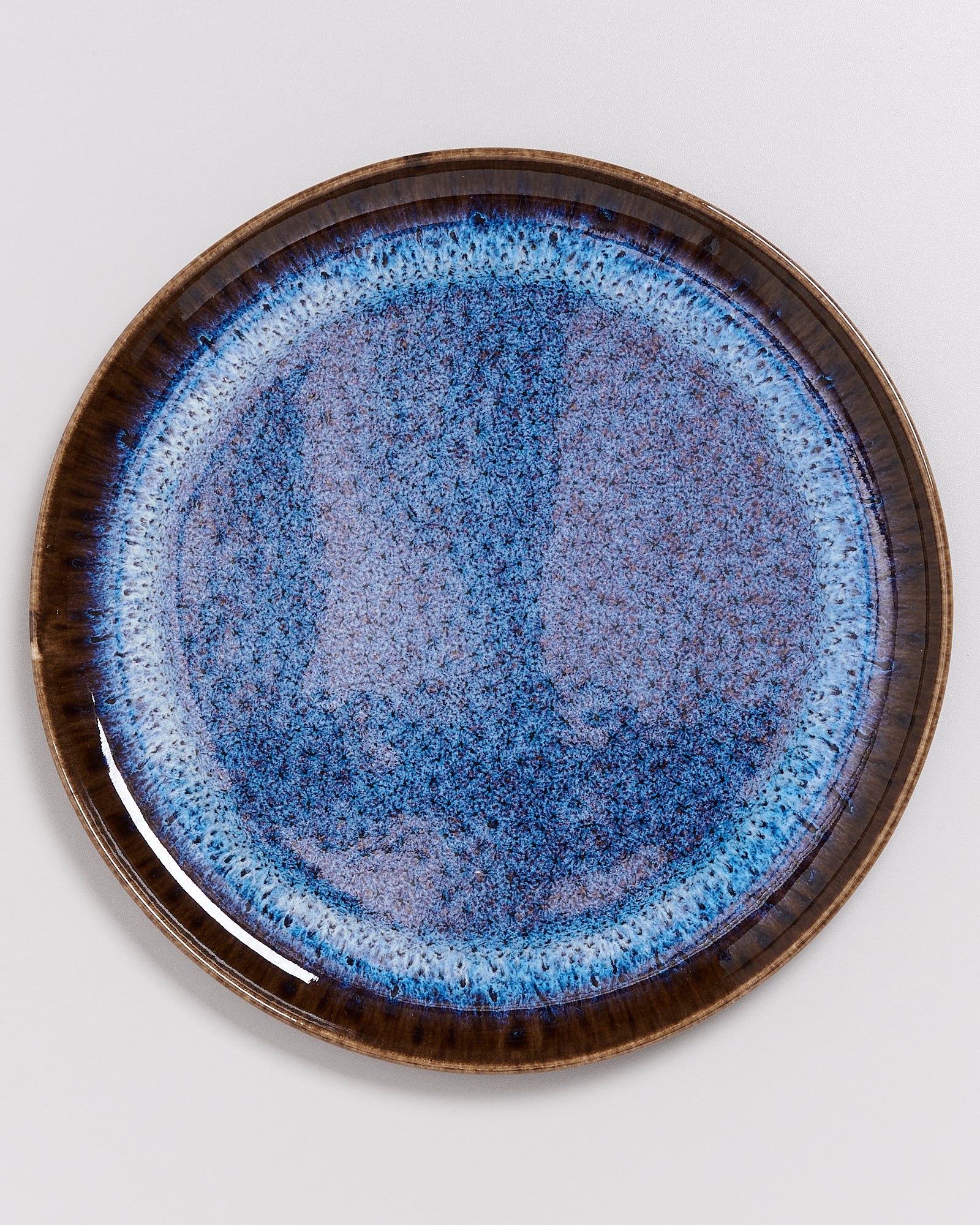 Blauer Keramikteller mit einem dunkelbraunen Rand und einer texturierten, marmorierten Oberfläche.