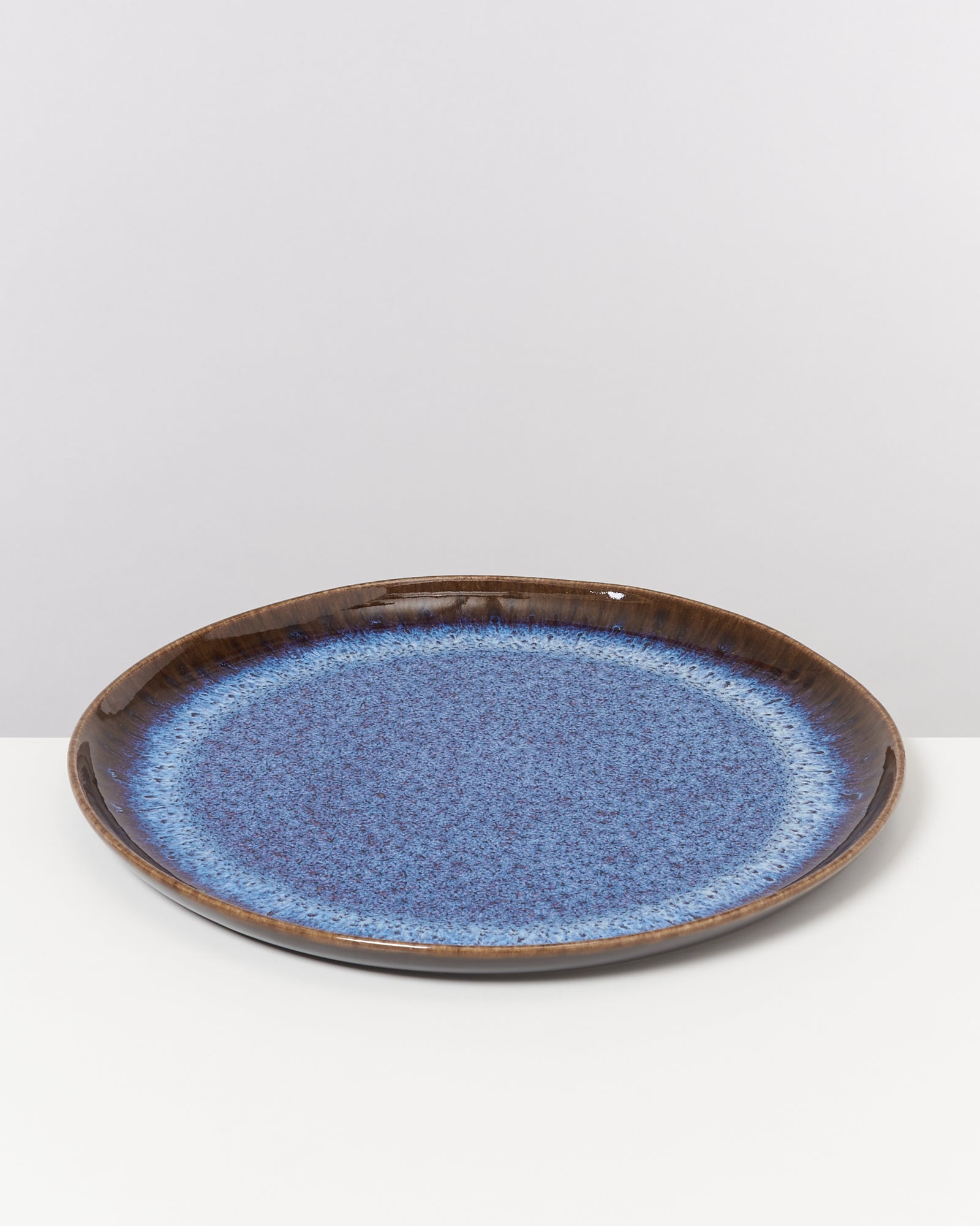 Brauner Teller mit blauer, gesprenkelter Glasur auf weißem Hintergrund.