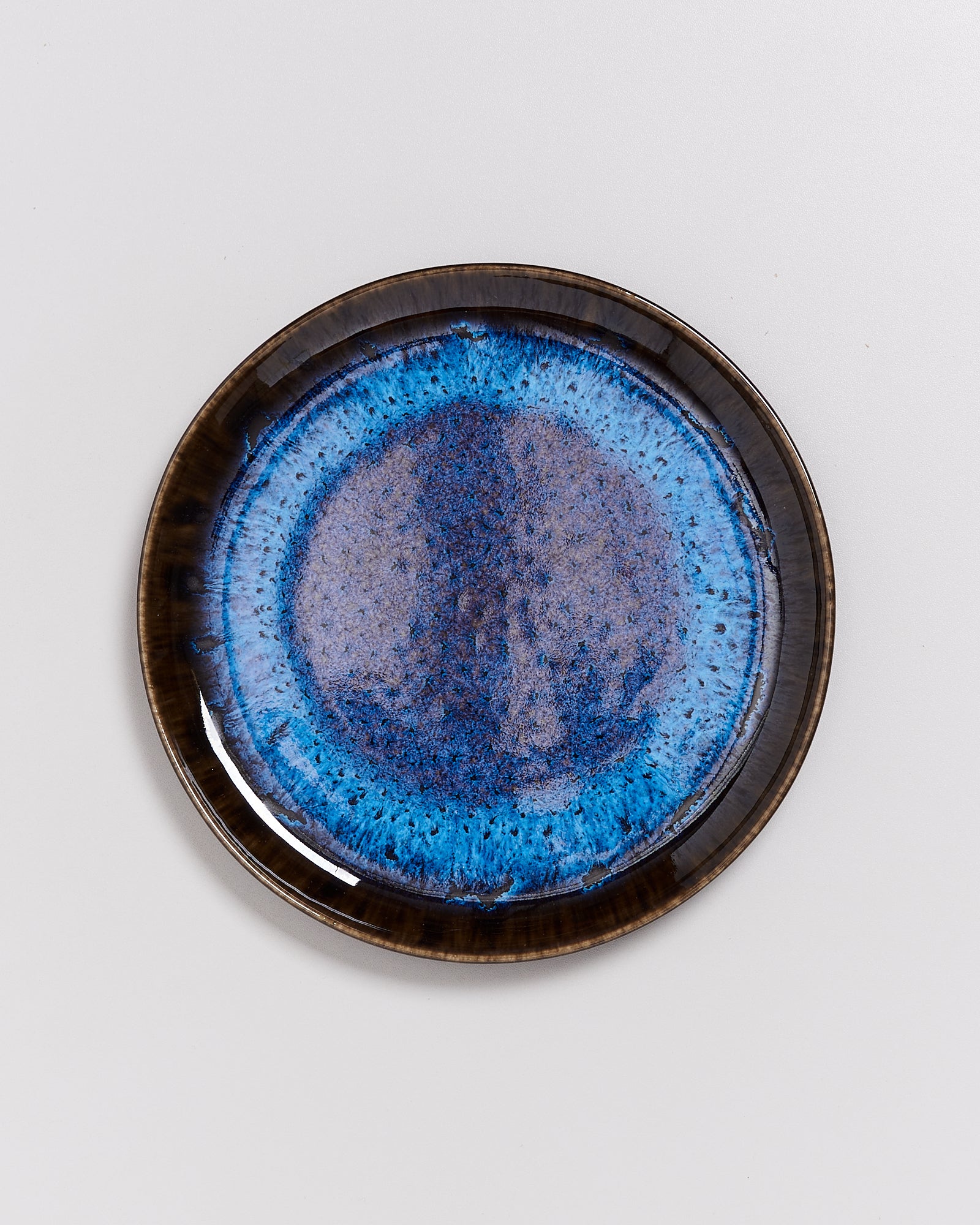 Blauer Keramikteller mit kunstvoller, gesprenkelter Glasur und braunem Rand auf weißem Hintergrund.