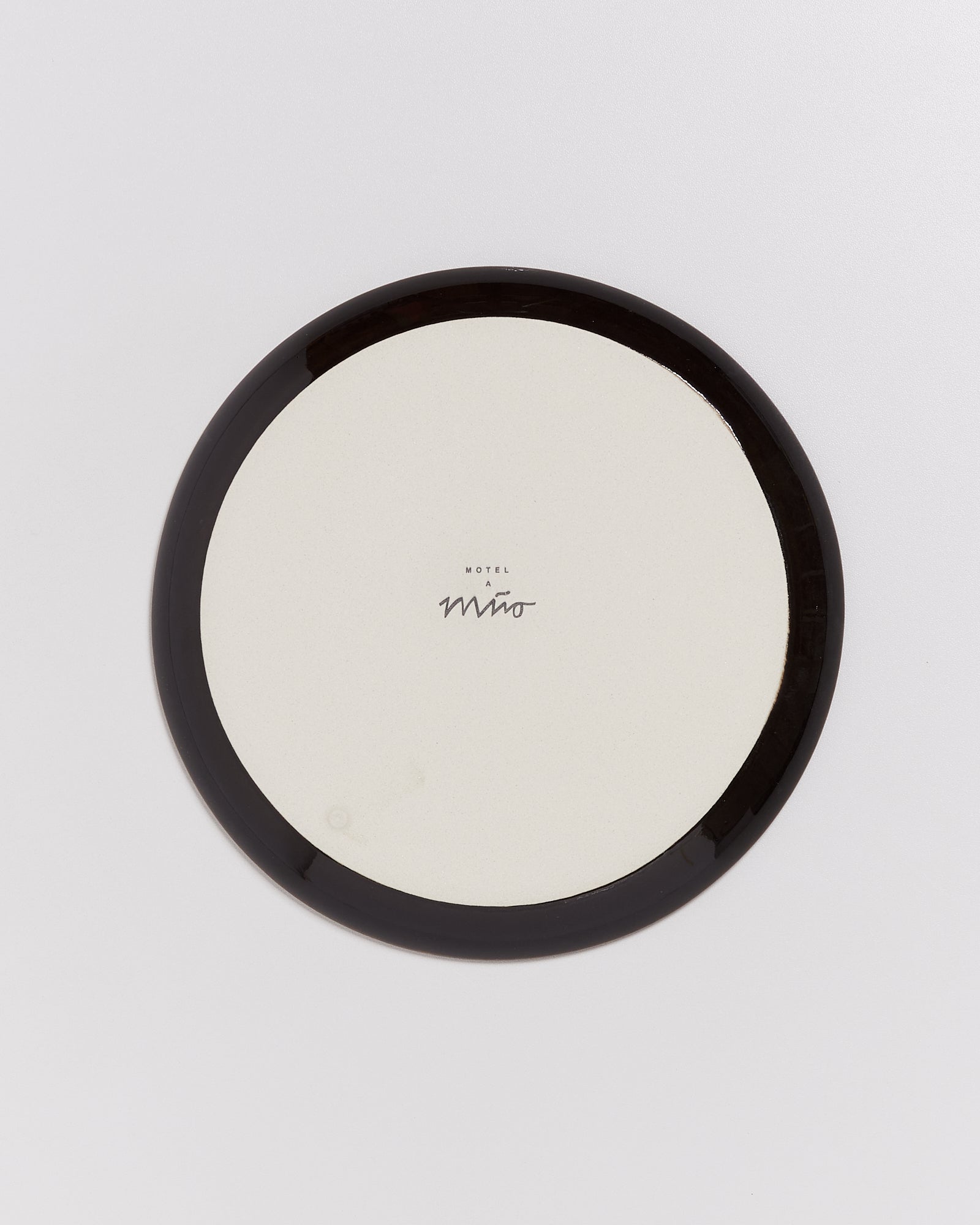 Runder Teller mit schwarzem Rand und der Aufschrift „Motel a Mio“ in der Mitte auf weißem Hintergrund.