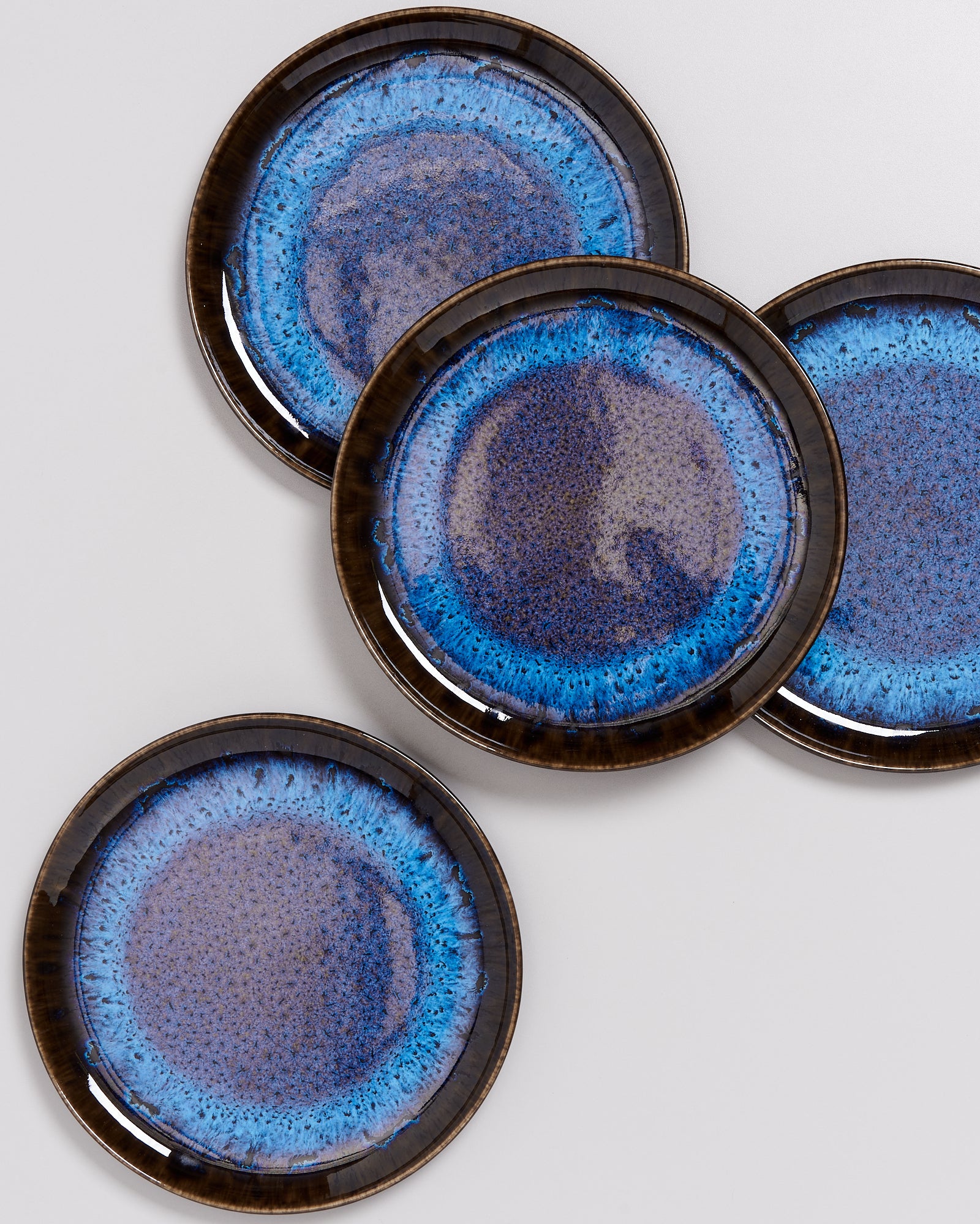 Vier runde Teller mit blau-schwarz glasiertem Rand liegen teilweise überlappend auf einer weißen Oberfläche.