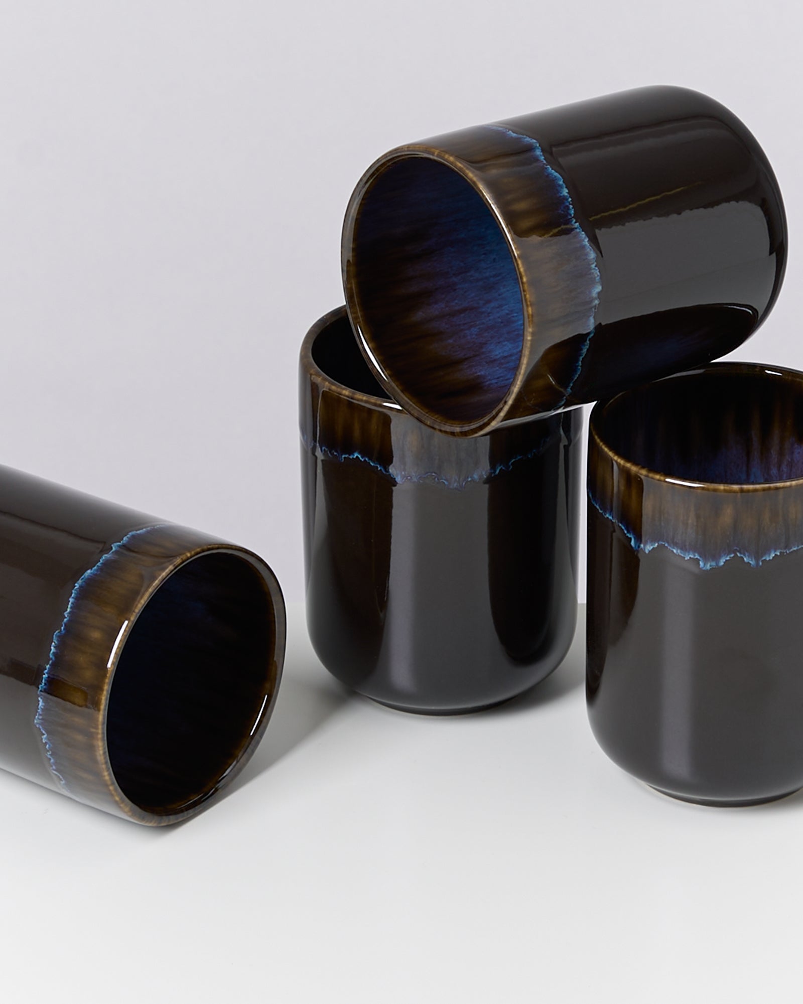 Vier schwarze Keramikbecher mit blauen und braunen Details auf einem grauen Hintergrund.