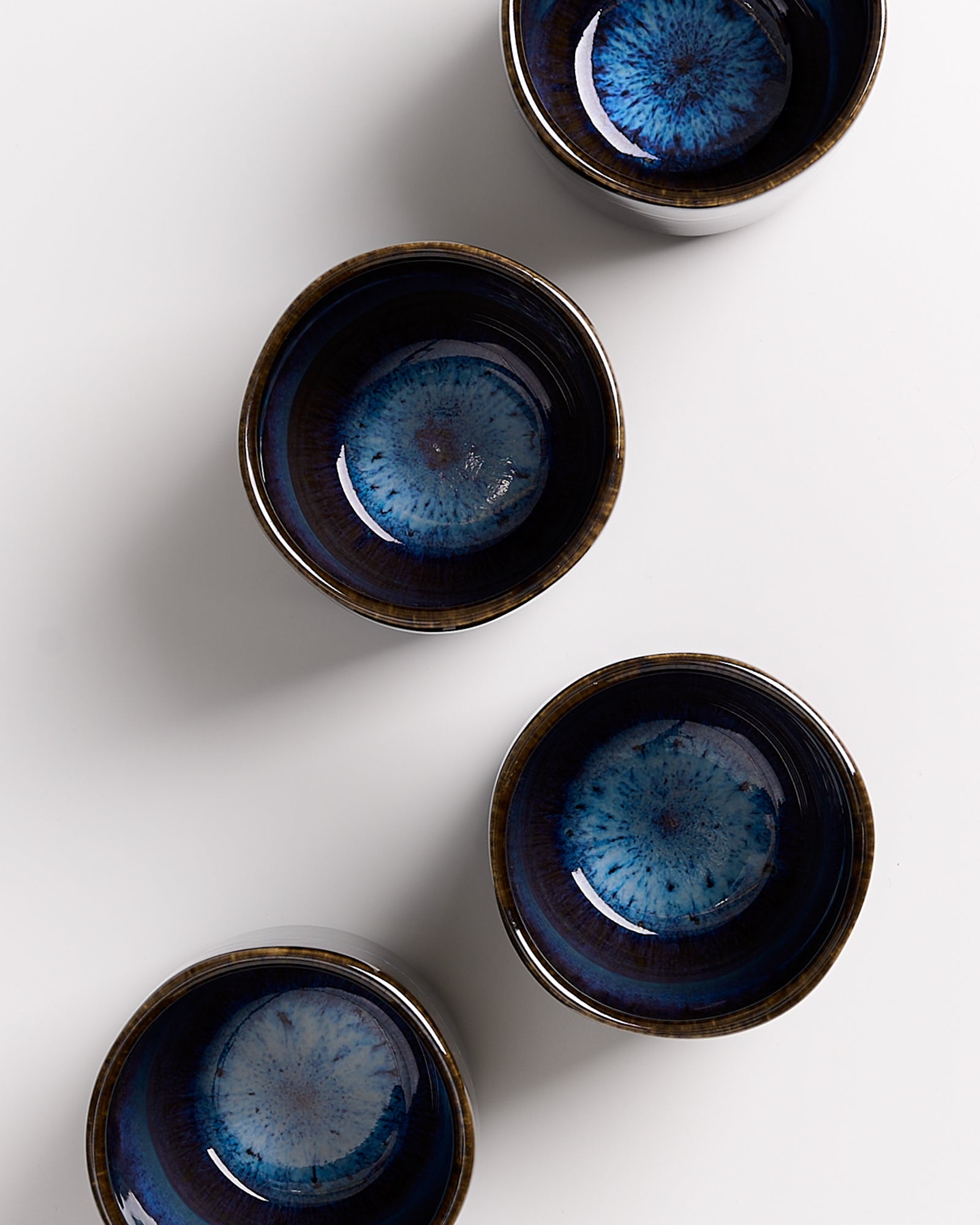 Vier blaue, glasierte Keramikschalen mit einem mandalaartigen Muster, auf weißem Hintergrund angeordnet.