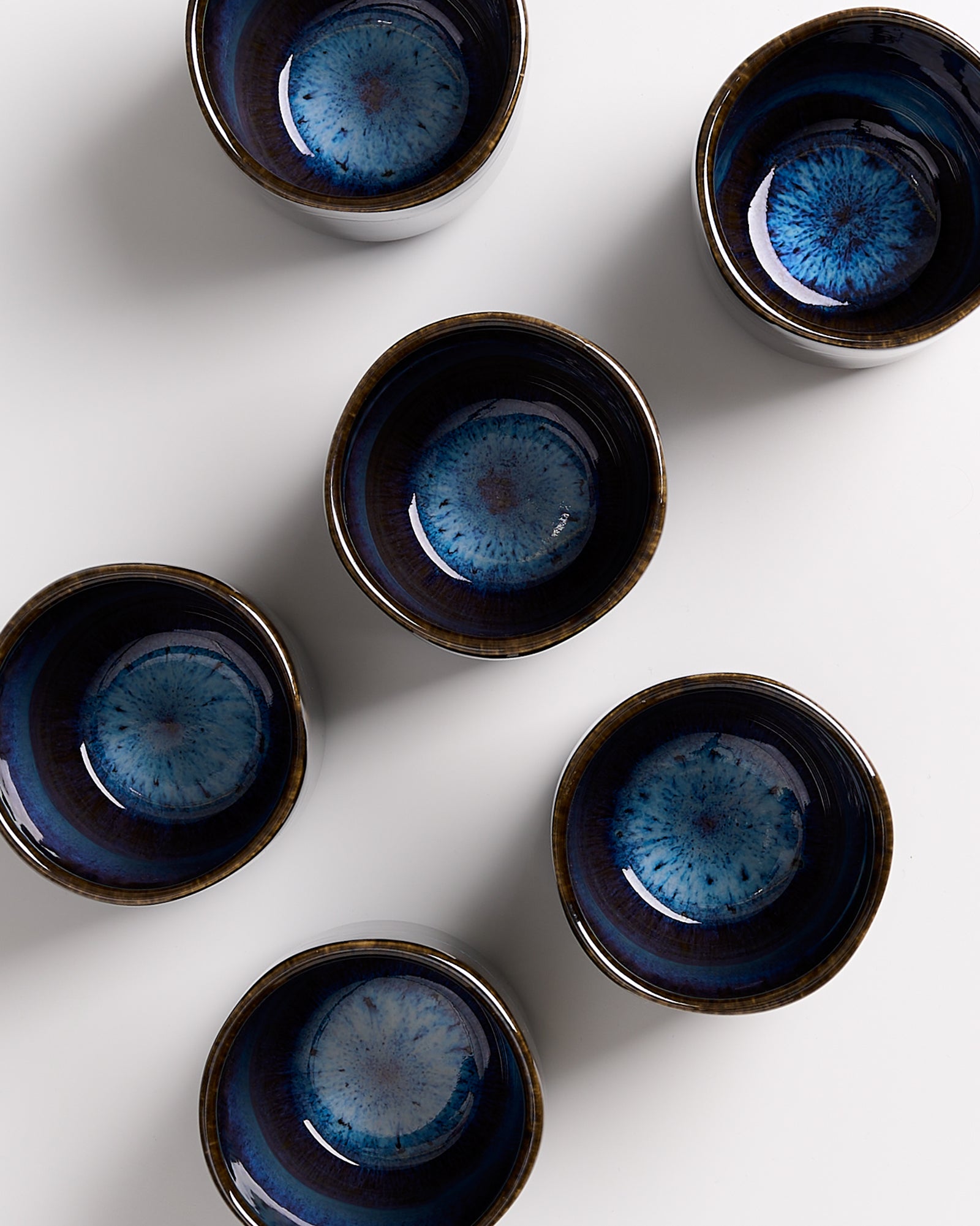 Sechs blaue, handgefertigte Keramikschalen mit Muster, von oben auf weißem Hintergrund gesehen.
