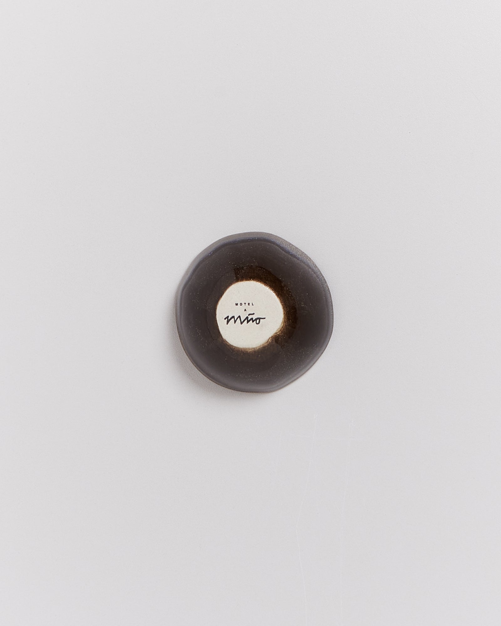 Runde, graue, flache Schale mit einem weißen Zentrum und dem Schriftzug "Hotel Miro", auf hellem Hintergrund.
