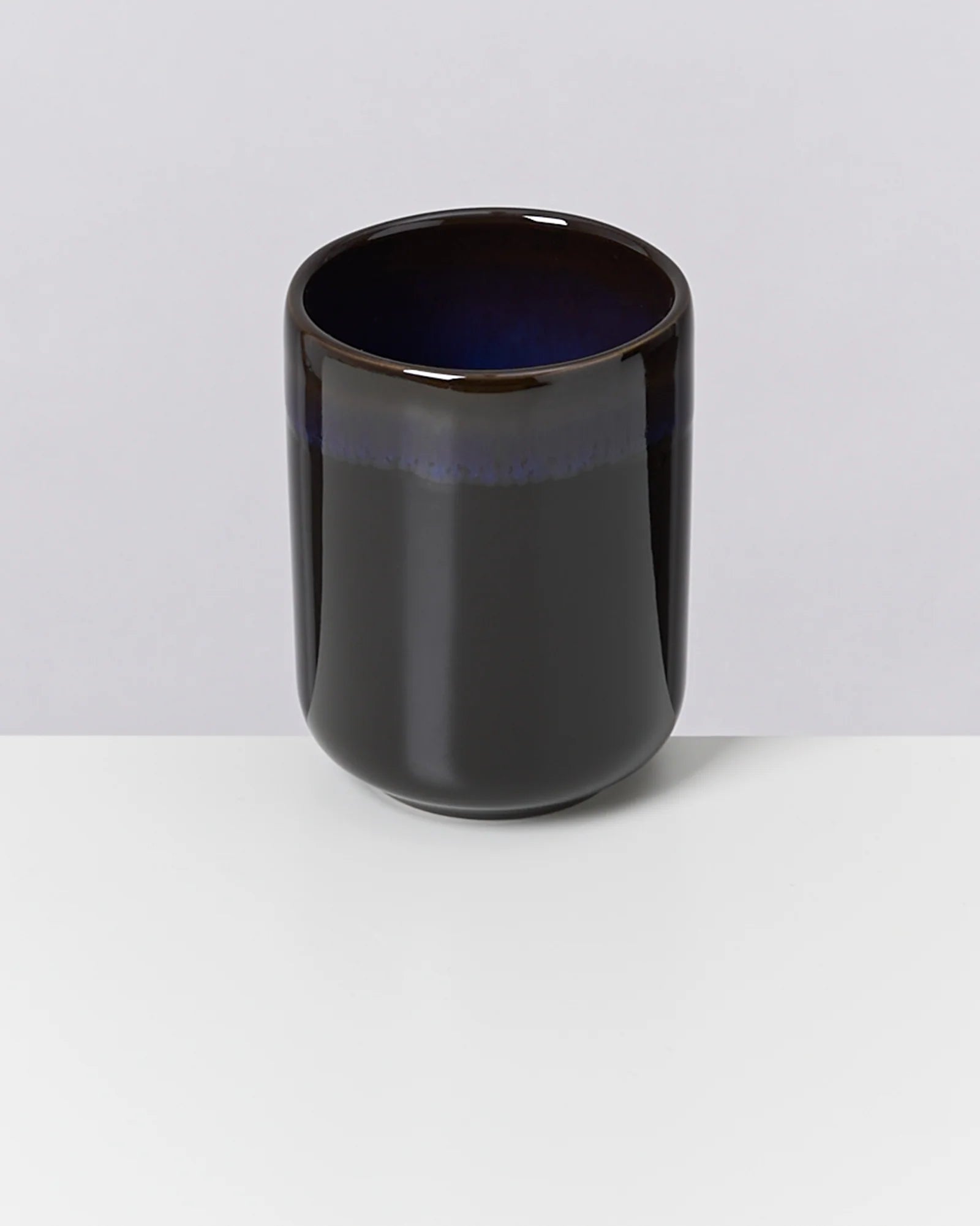 Dunkle, glänzende Tasse mit blauem Innenrand steht auf einem weißen Untergrund.