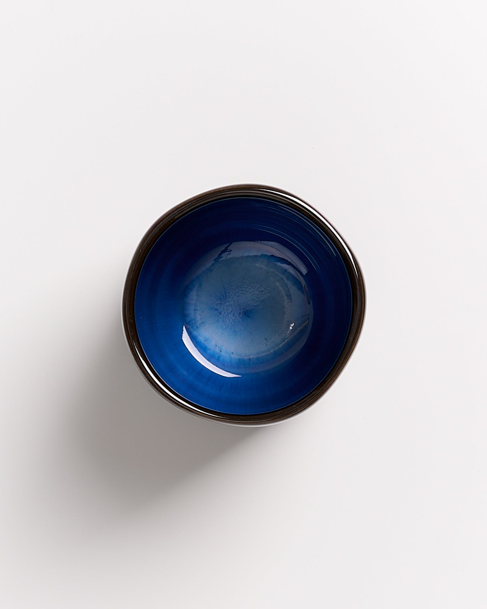 Blaue Schüssel mit dunklem Rand auf weißem Hintergrund, von oben betrachtet.