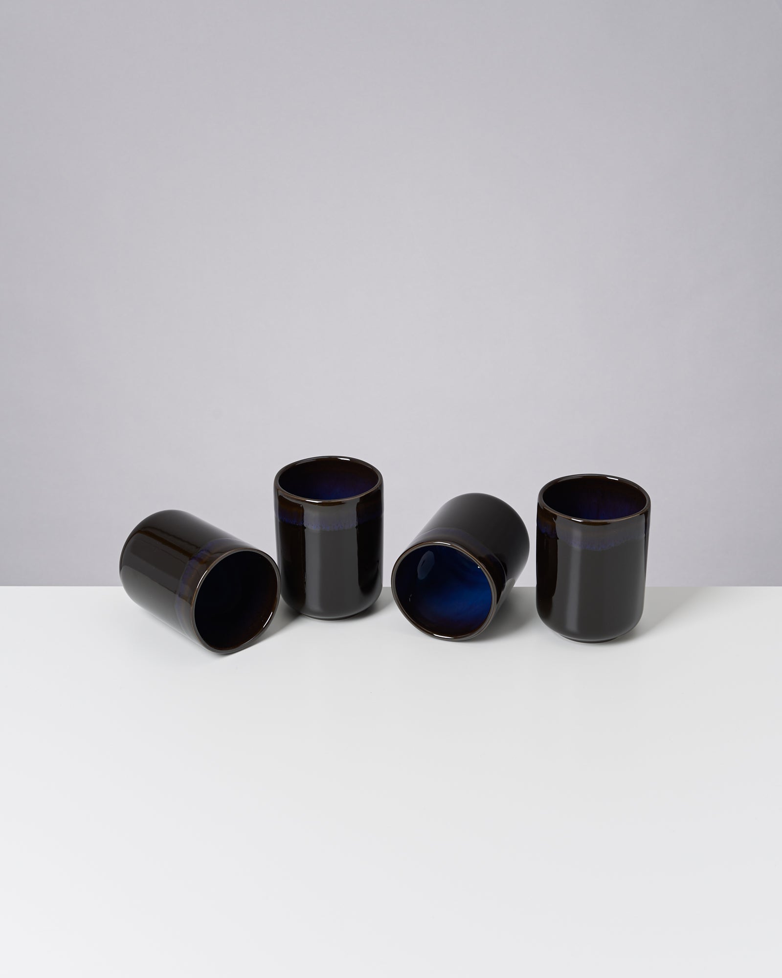 Vier schwarze Tassen mit blauer Innenfarbe stehen auf einem weißen Tisch.