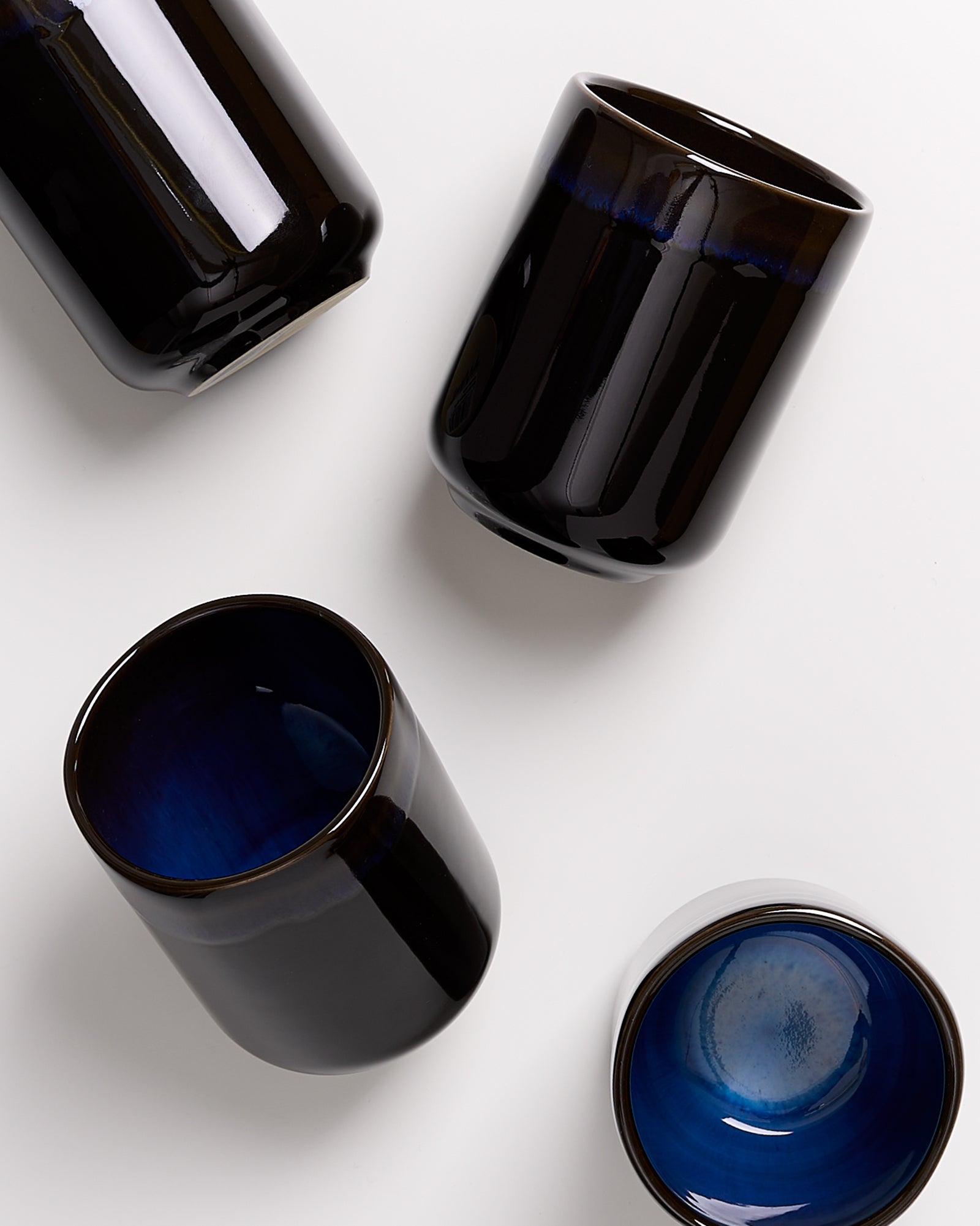Vier schwarze Keramiktassen mit blauer Innenfläche auf weißem Hintergrund.