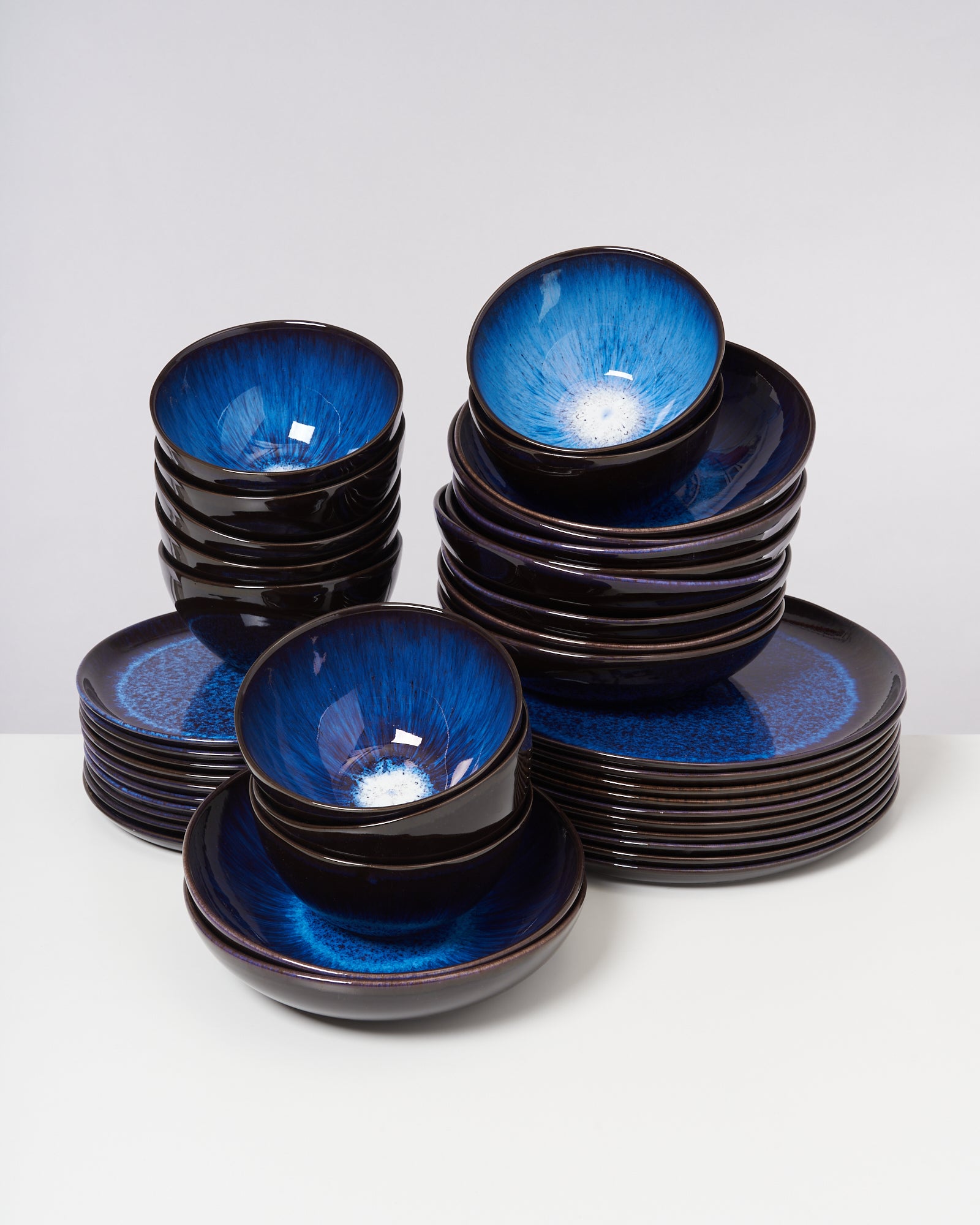 Mehrere gestapelte blaue Keramikschalen und -teller mit glänzender Glasur auf einer weißen Oberfläche.