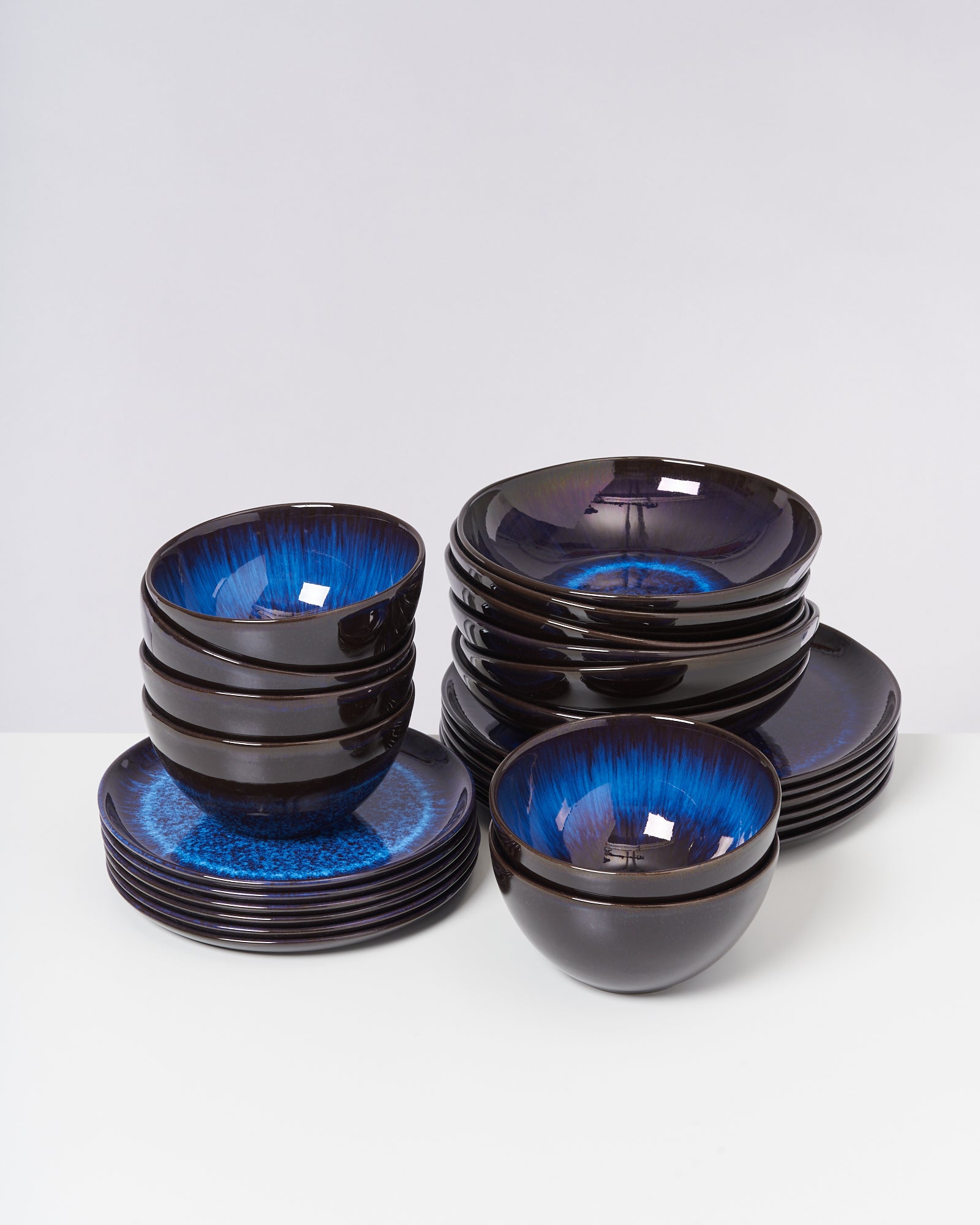 Verschiedene gestapelte schwarze Schüsseln und Teller mit leuchtend blauer Glasur auf einem weißen Hintergrund.