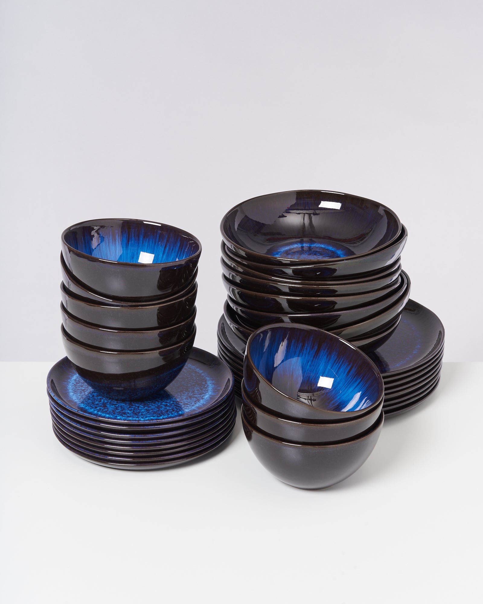 Ein Stapel schwarzer Schüsseln und Teller mit blauem Innenmuster auf weißem Hintergrund.