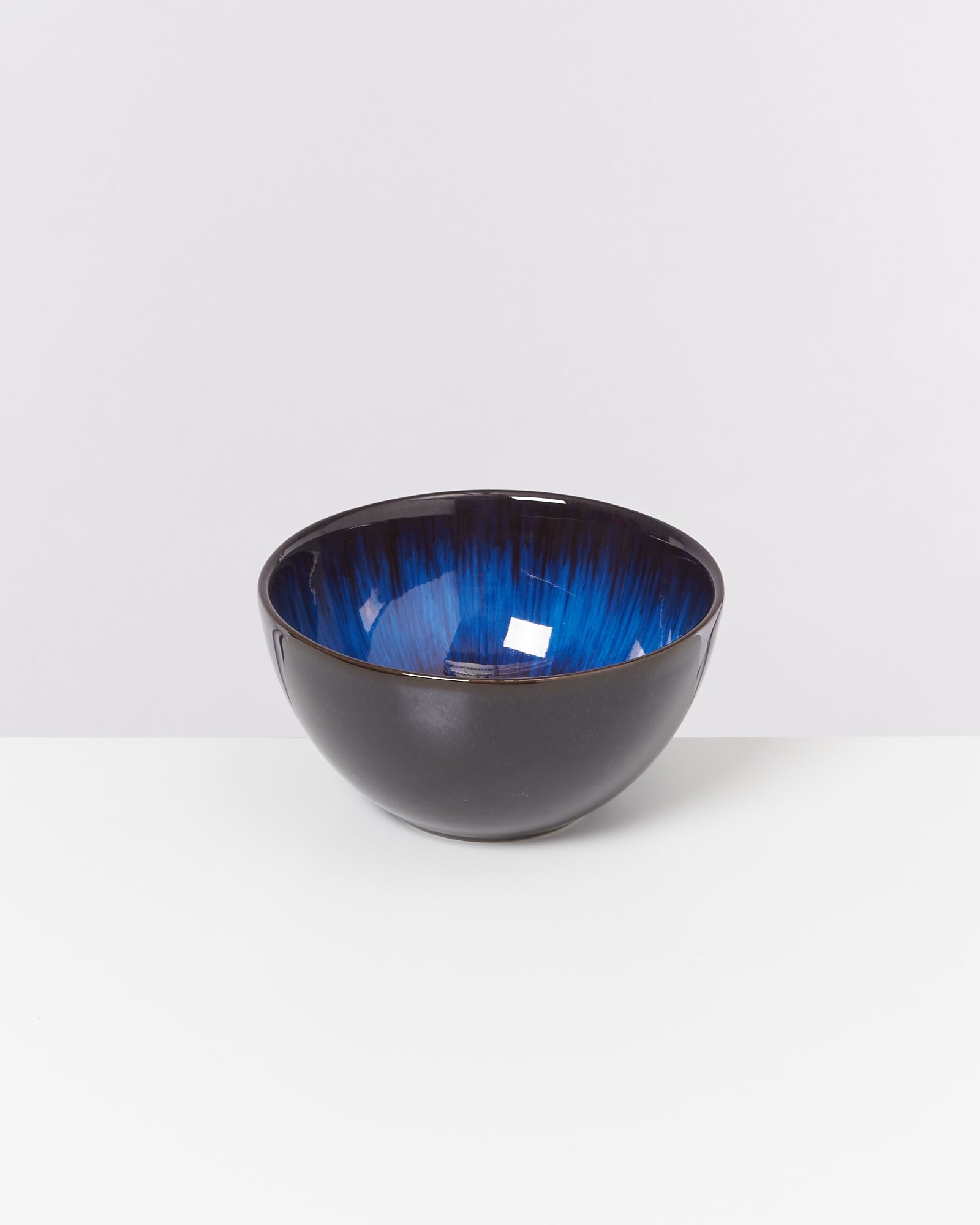 Schwarze Keramikschale mit blauem, glänzendem Innenbereich auf weißem Hintergrund.