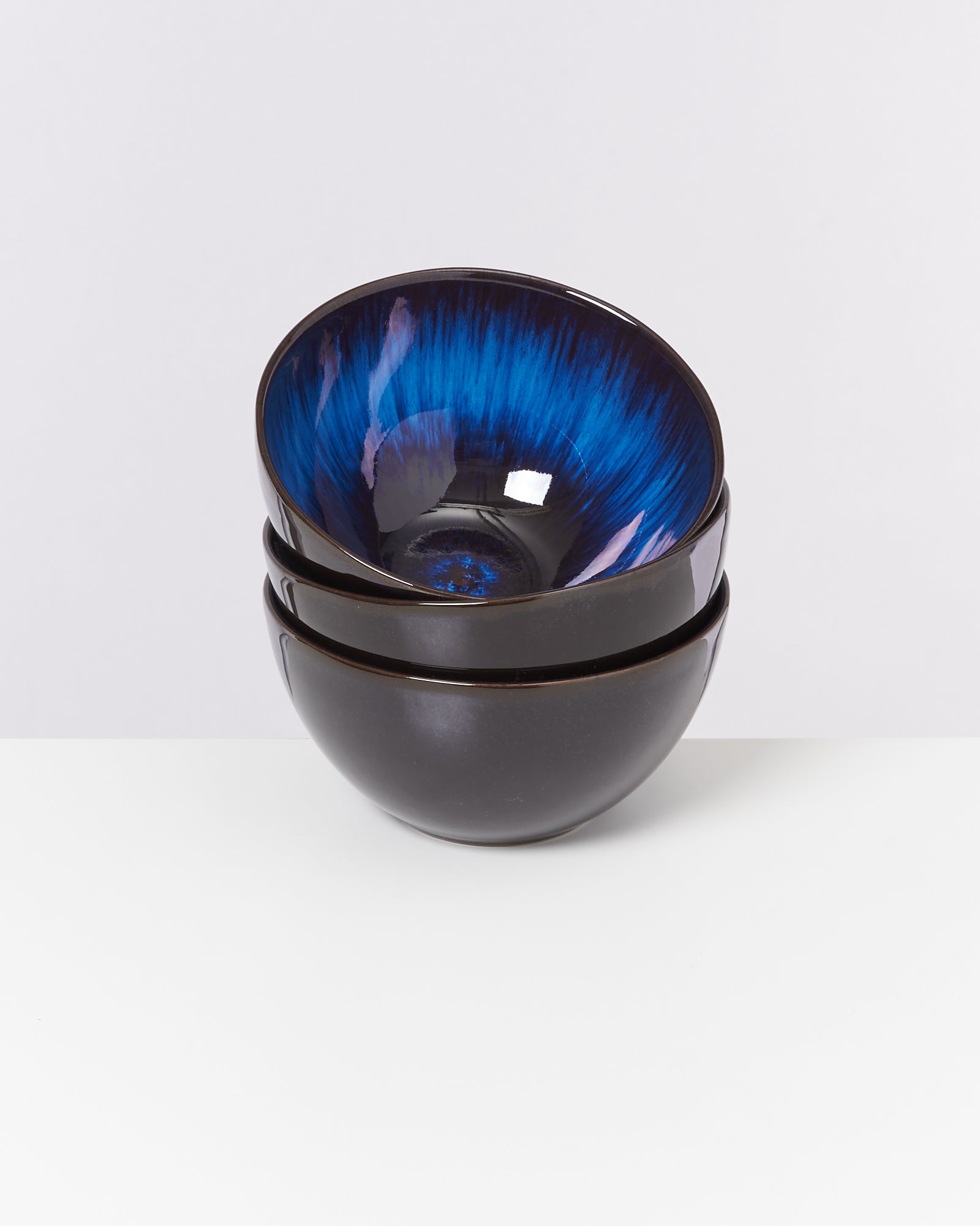 Drei ineinander gestapelte, schwarze Schalen mit einem leuchtend blauen Innenmuster auf weißem Hintergrund.