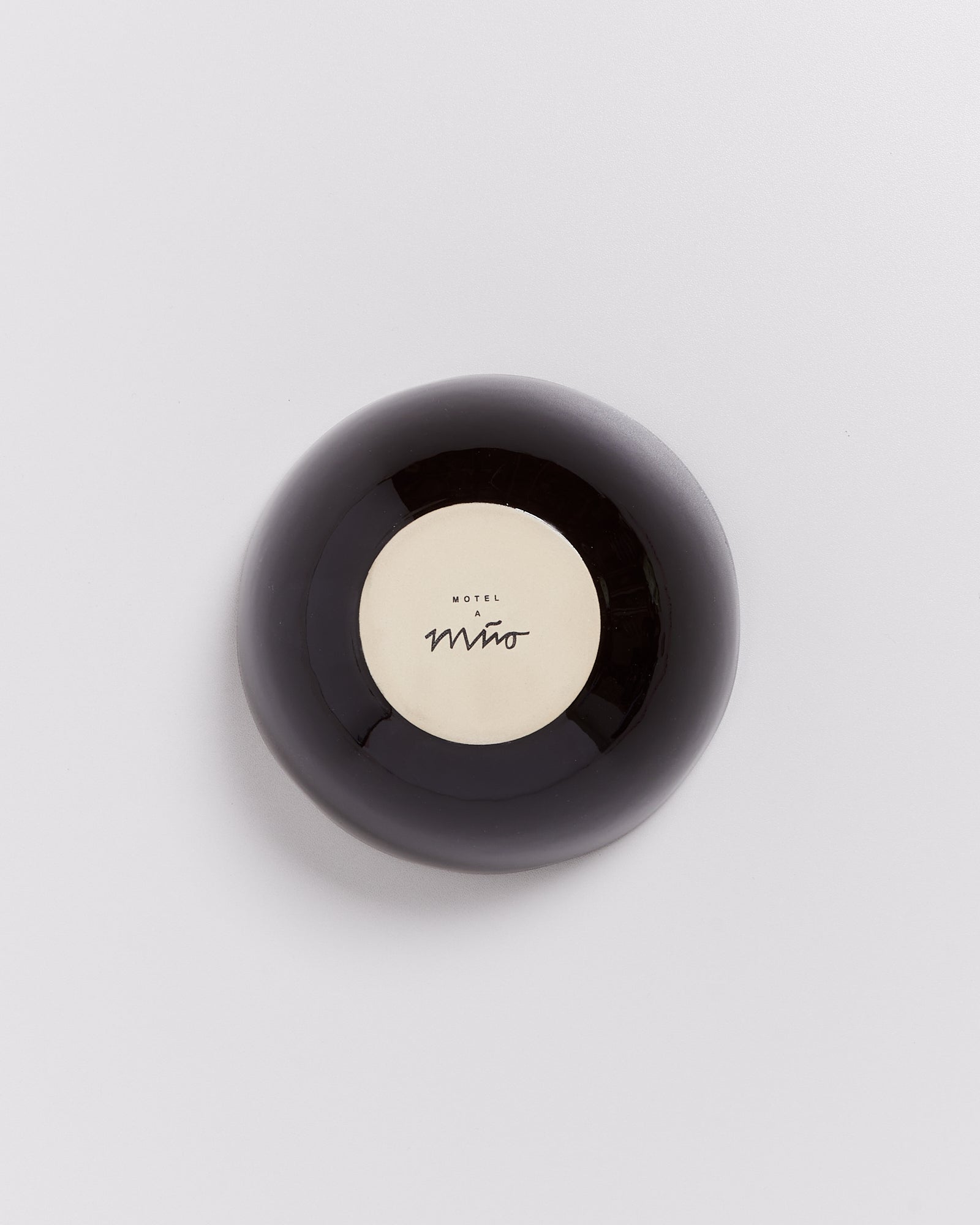 Schwarze, runde Gegenstand mit beiger Mitte und der Aufschrift "Motel a Miio" auf hellem Hintergrund.