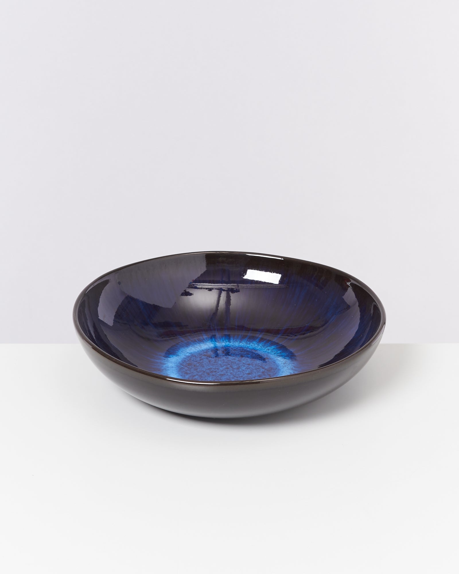 Schwarze Schale mit glänzendem, blau gefärbtem Inneren auf einem weißen Hintergrund.