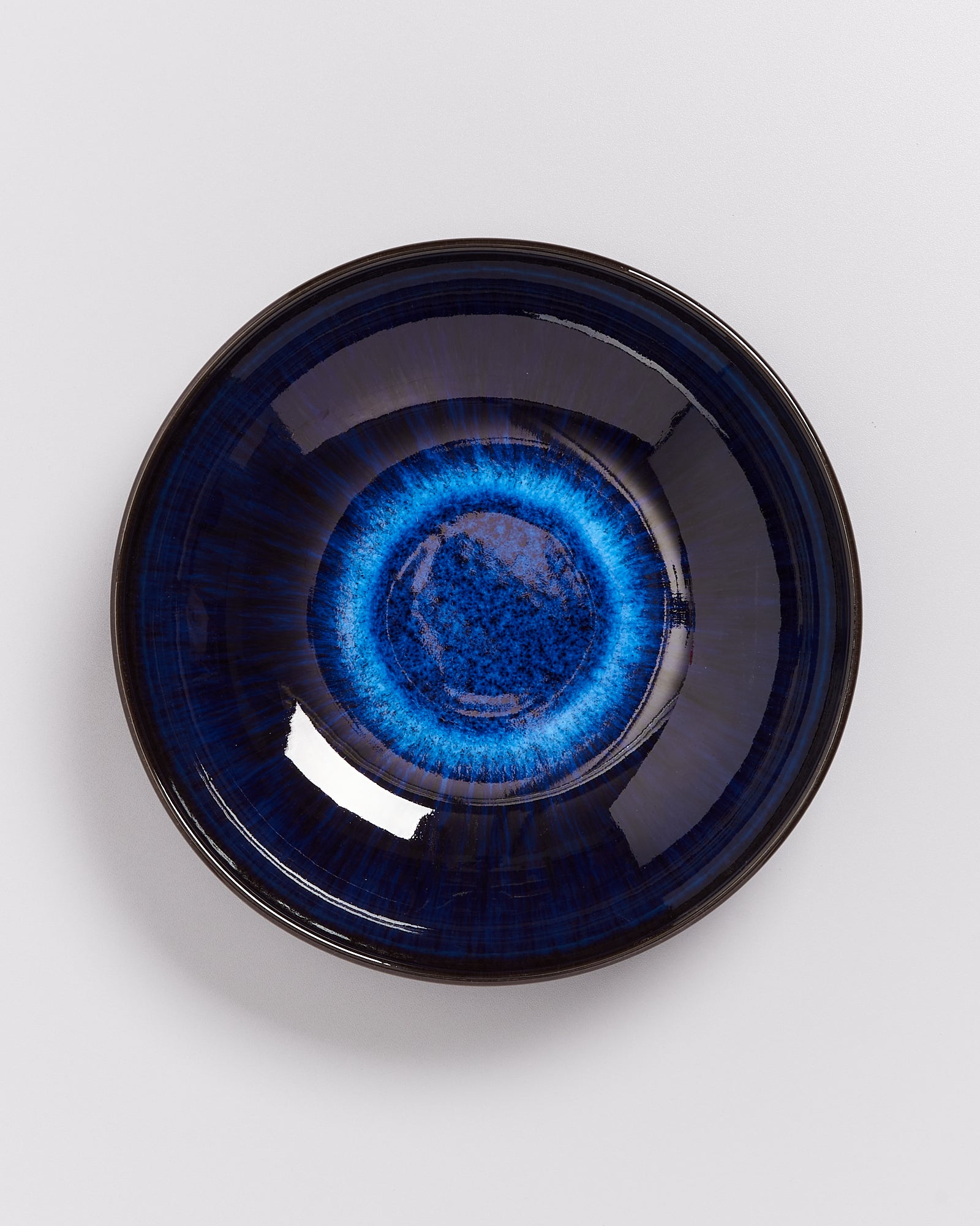 Dunkelblaue, glänzende Keramikschale mit einem helleren blauen Ring in der Mitte auf weißem Hintergrund.