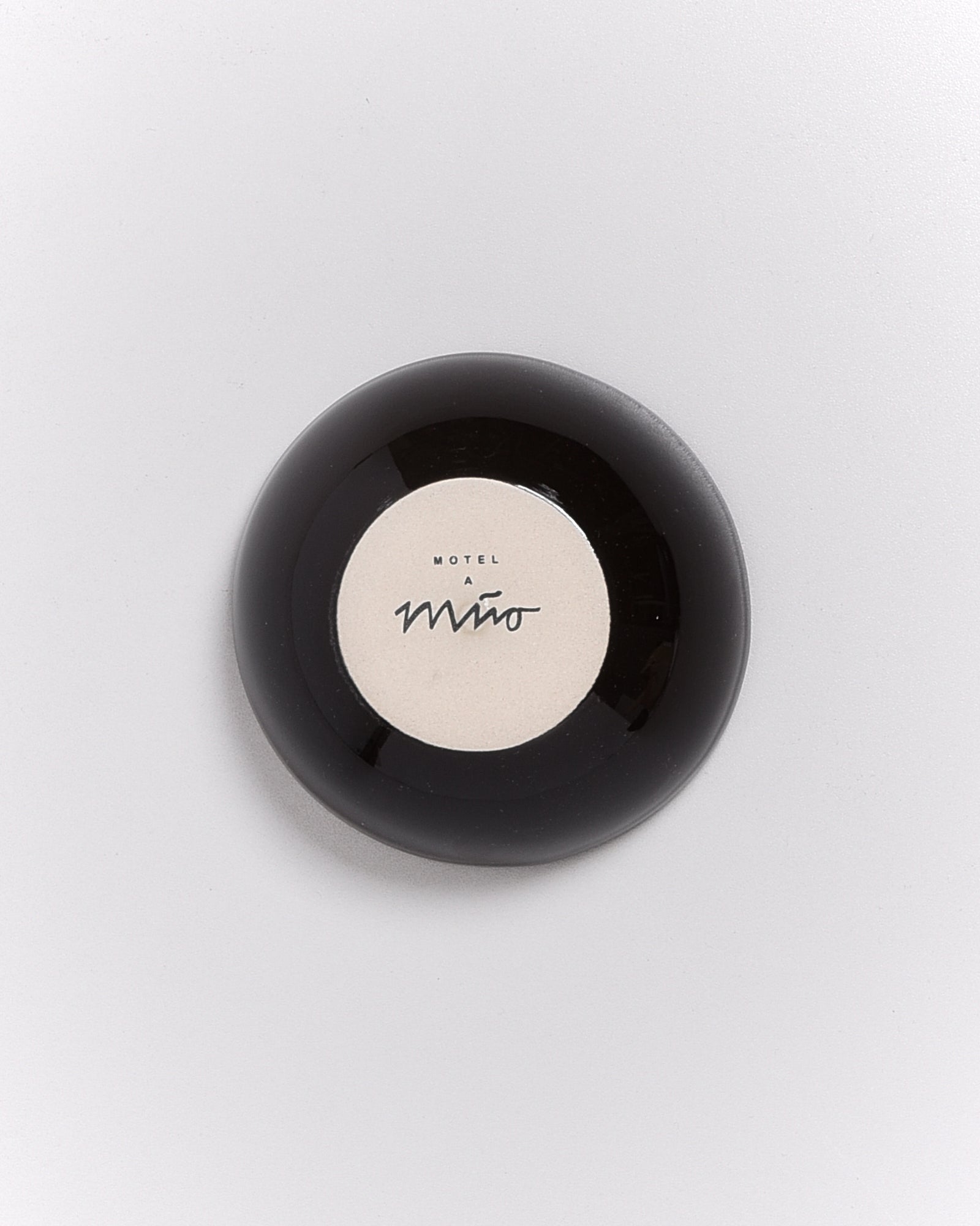 Rundes schwarzes Objekt mit der Aufschrift „Motel A Miro“ auf beige Hintergrund.