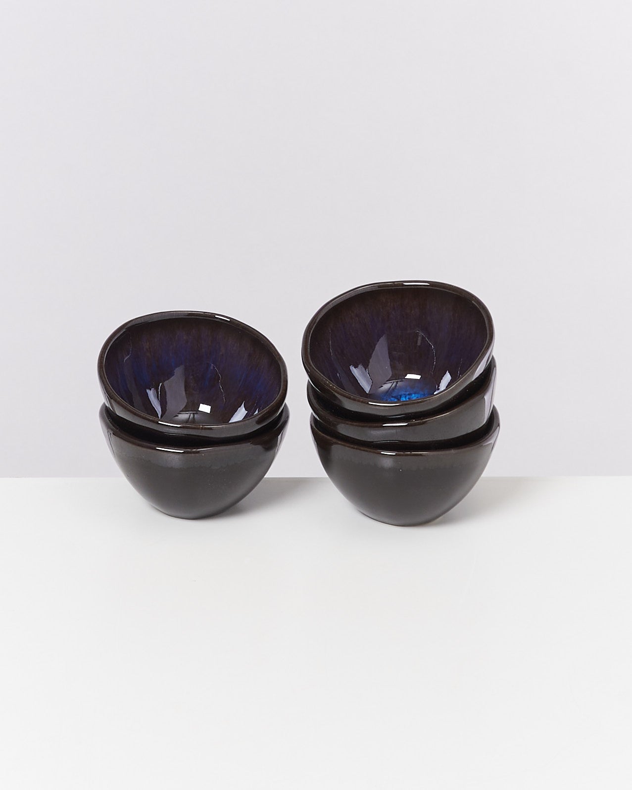 Vier gestapelte schwarze Schalen mit glänzendem blauen Inneren auf weißem Hintergrund.