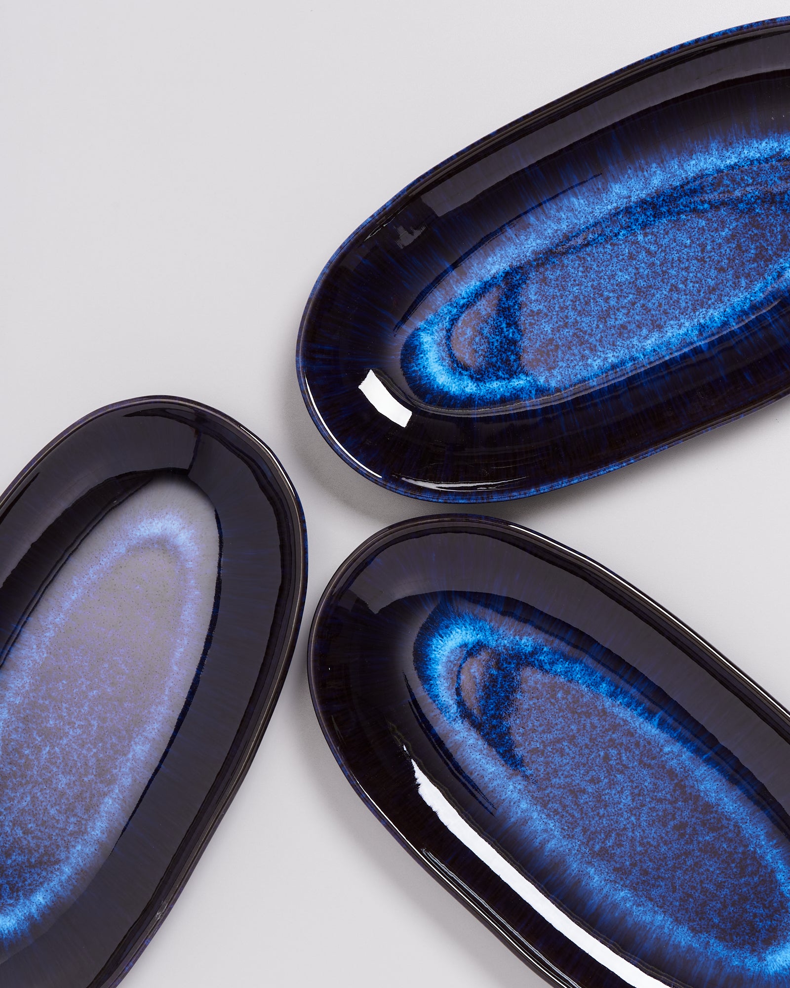 Drei ovale, blaue Teller mit einem leuchtenden Randdesign auf hellem Hintergrund.