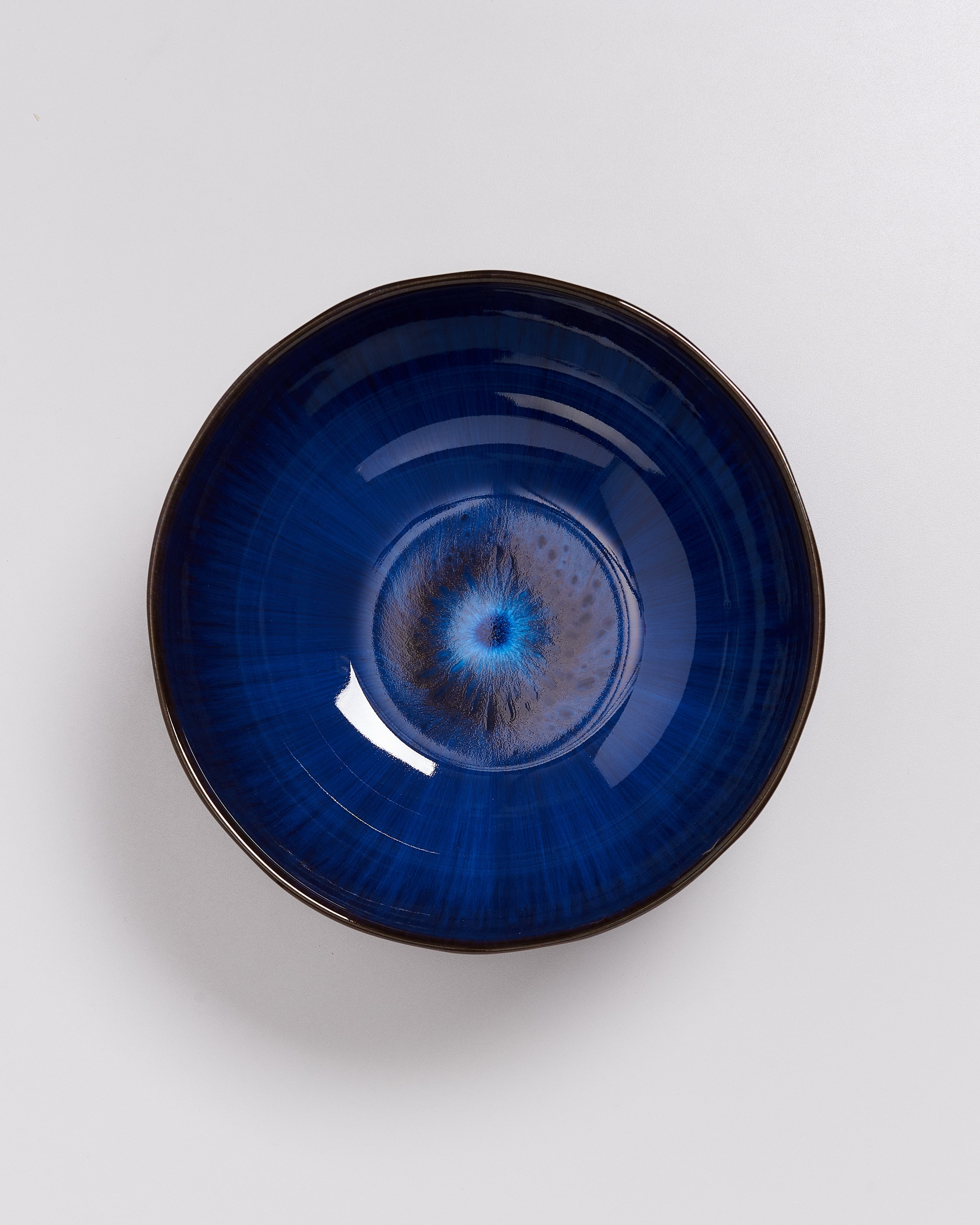 Blau-glasierte Schale mit einem konzentrisch-kreisförmigen Muster in der Mitte, auf weißem Hintergrund.