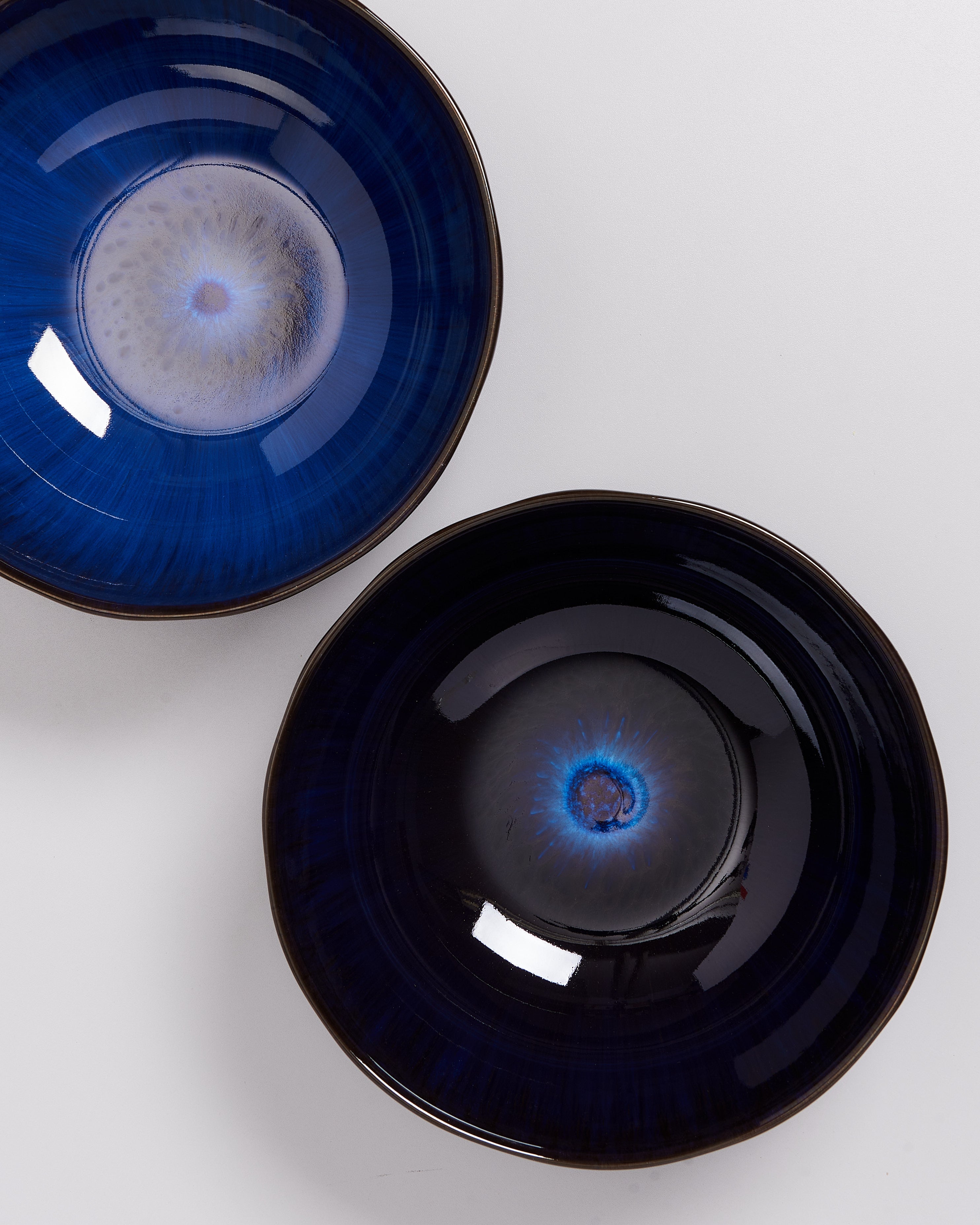 Zwei dunkle, blau glasierte Schüsseln mit einem leuchtenden Muster in der Mitte auf einem weißen Hintergrund.