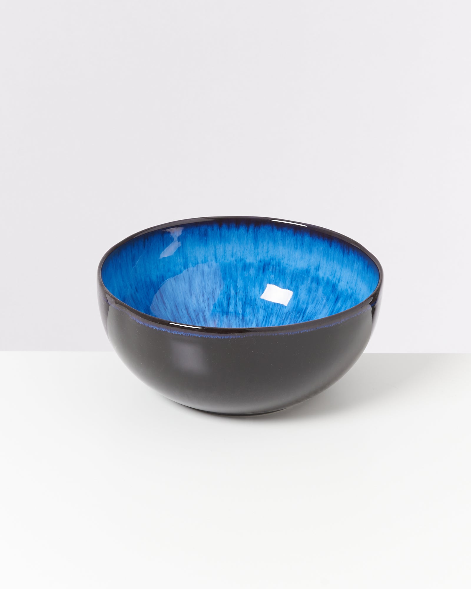 Schwarze Schale mit glänzender blauer Innenseite auf weißem Hintergrund.