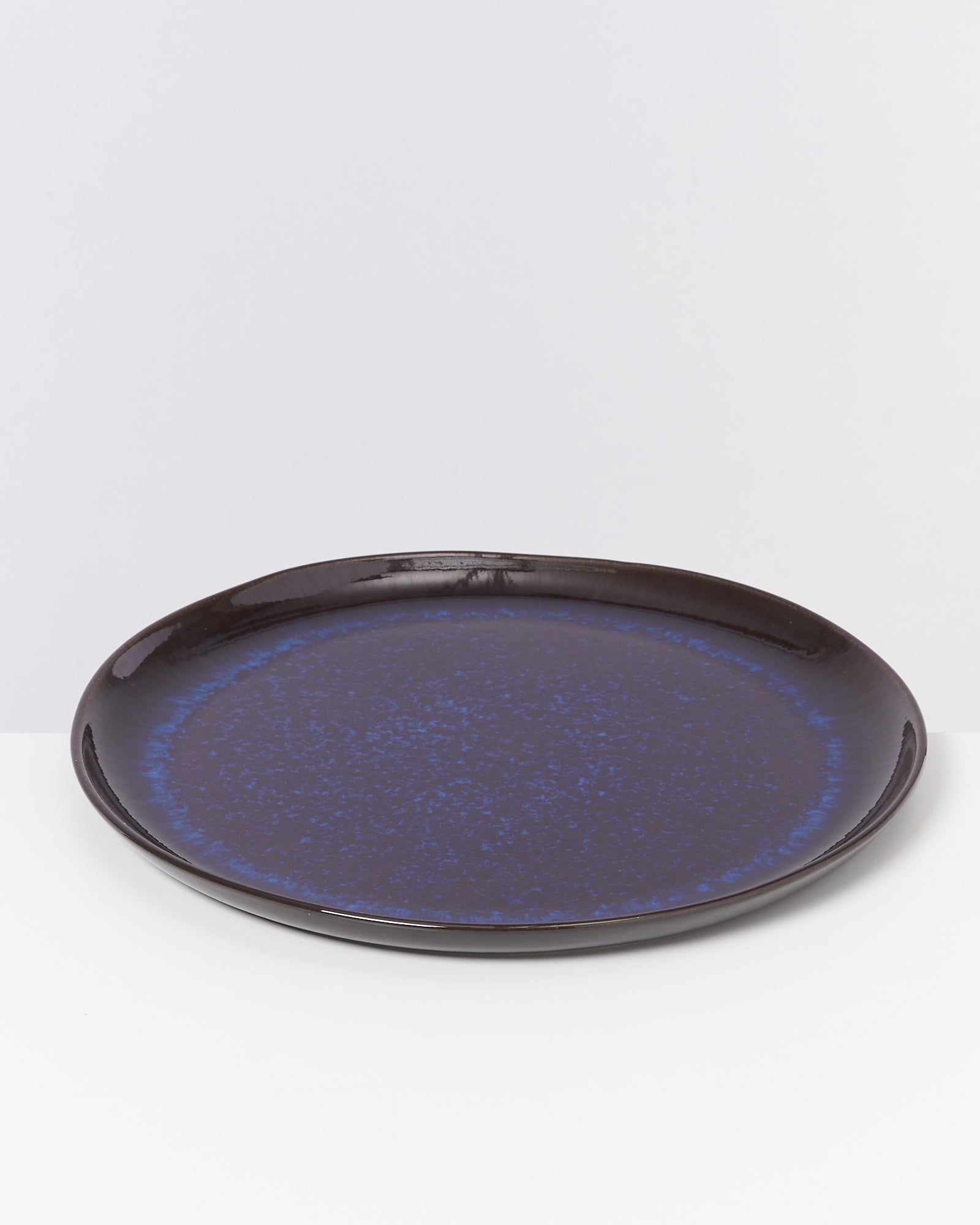 Ein runder, dunkelblauer Teller mit leichtem Glanz steht auf einer weißen Oberfläche.