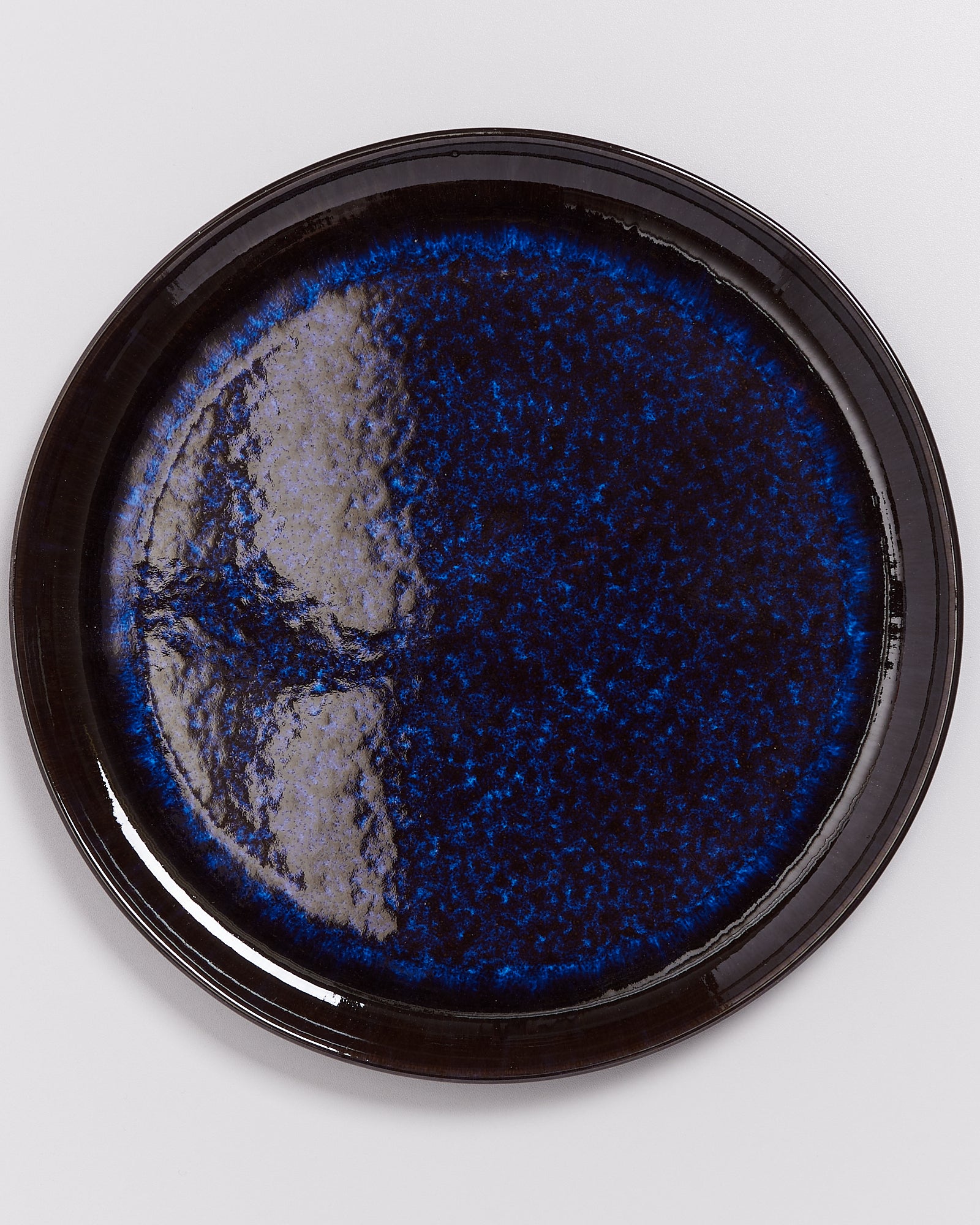 Runder, tiefblauer Keramikteller mit glänzender Oberfläche auf weißem Hintergrund.