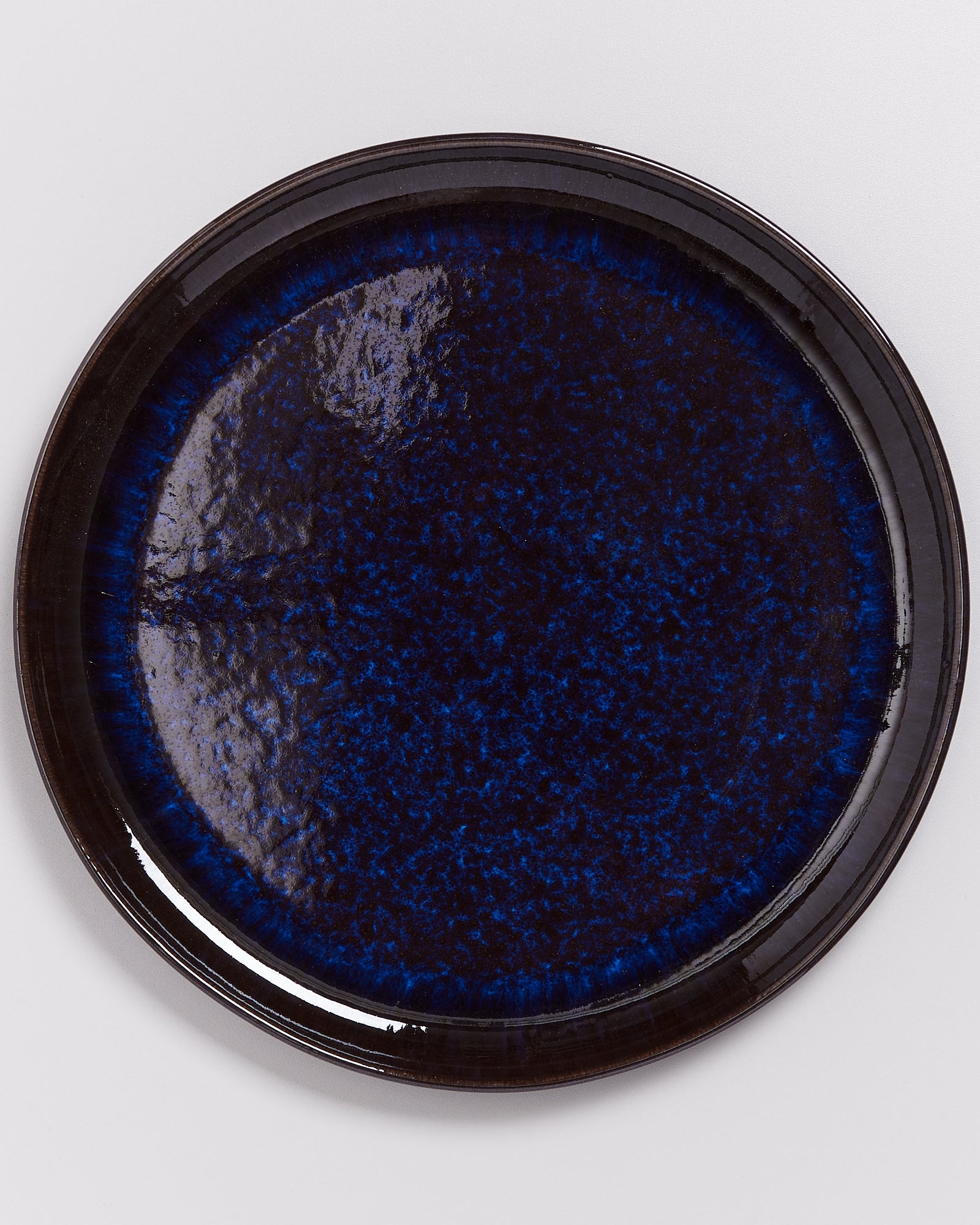 Runder, dunkelblauer Keramikteller mit gesprenkeltem Muster auf einer weißen Oberfläche.