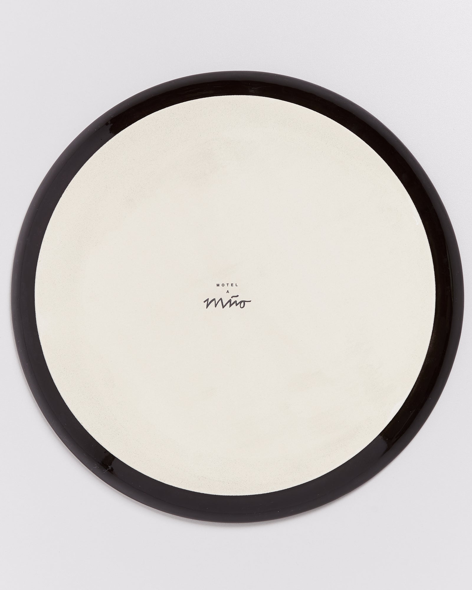Ein runder Teller mit schwarzem Rand und der Aufschrift "Motel a Miio" in der Mitte.
