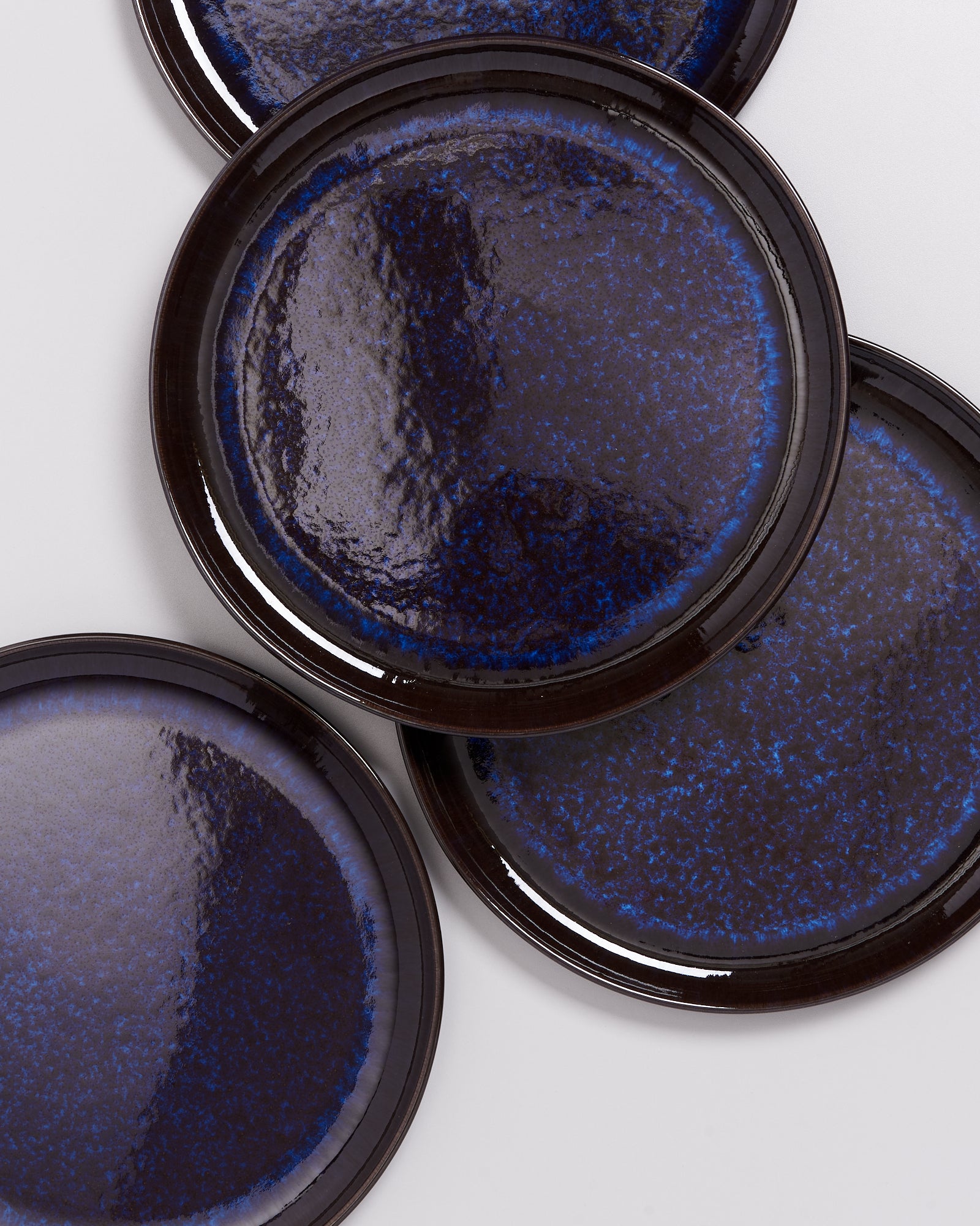 Vier überlappende, tiefblaue Keramikteller mit glänzender Oberfläche auf hellem Hintergrund.