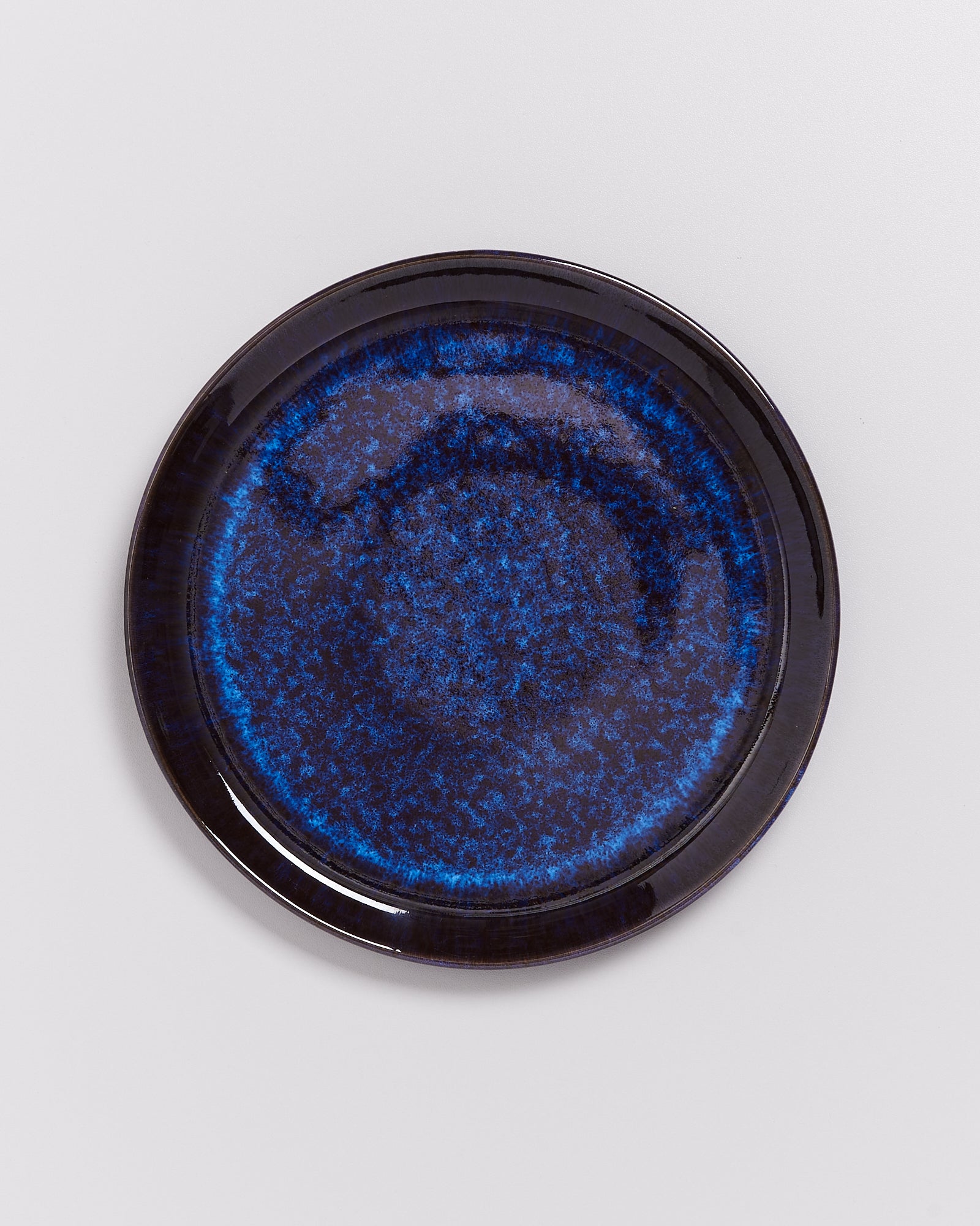 Dunkelblauer Keramikteller mit gesprenkeltem Muster auf weißem Hintergrund.
