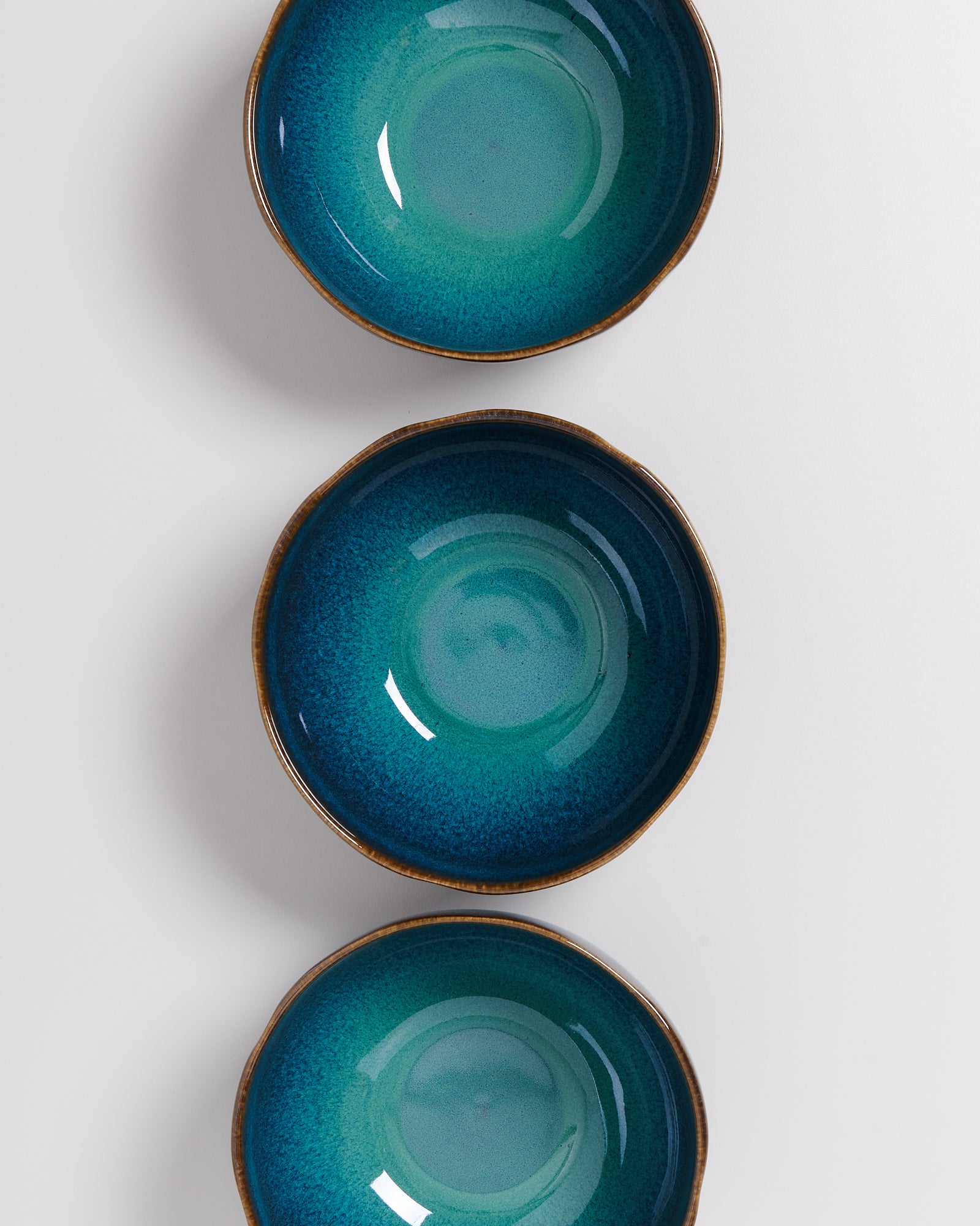 Drei türkisblaue Keramikschalen mit braunem Rand auf weißem Hintergrund, in einer vertikalen Reihe angeordnet.