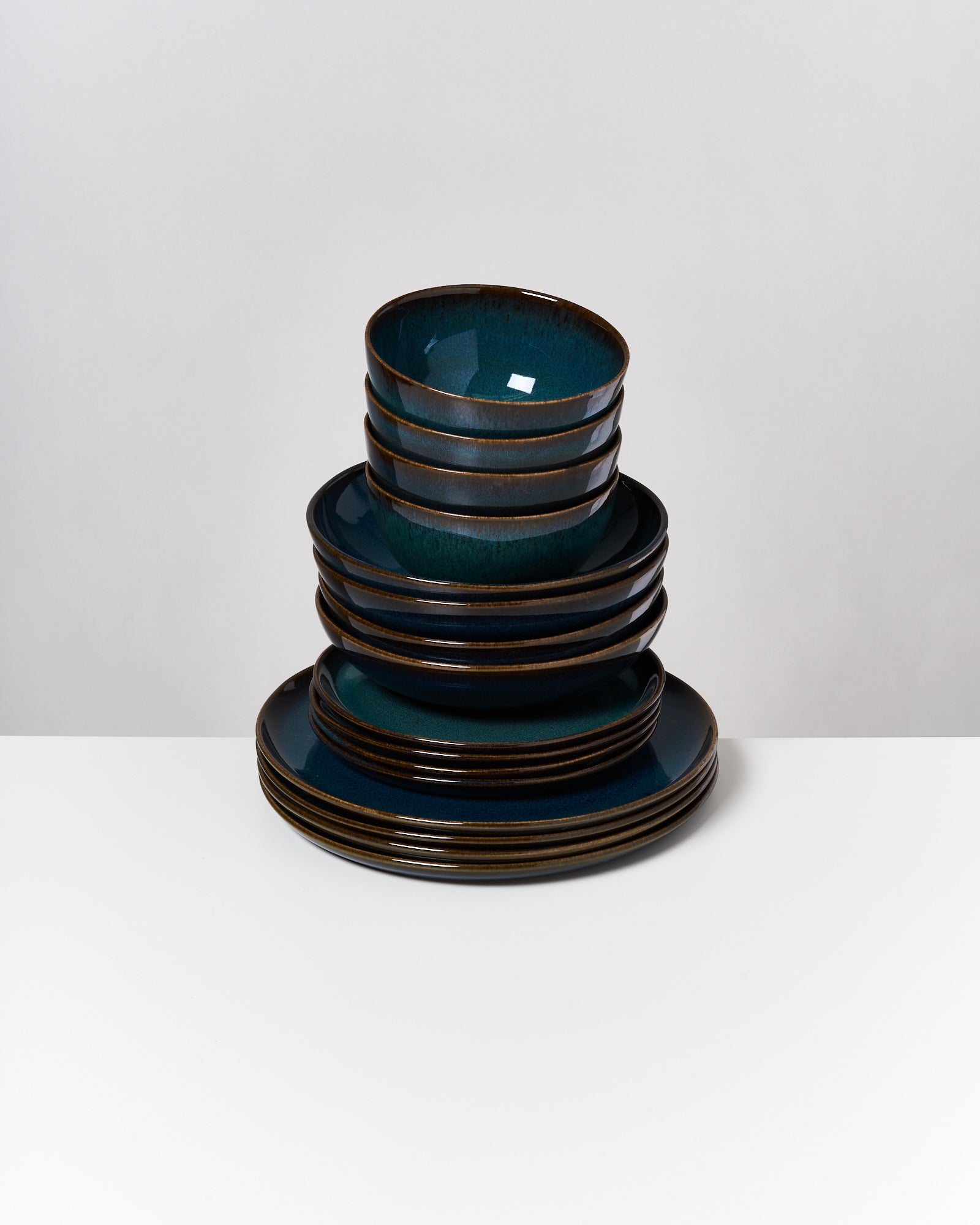 Ein Stapel aus dunkelblauen Tellern und Schalen steht auf einem weißen Tisch vor einem grauen Hintergrund.