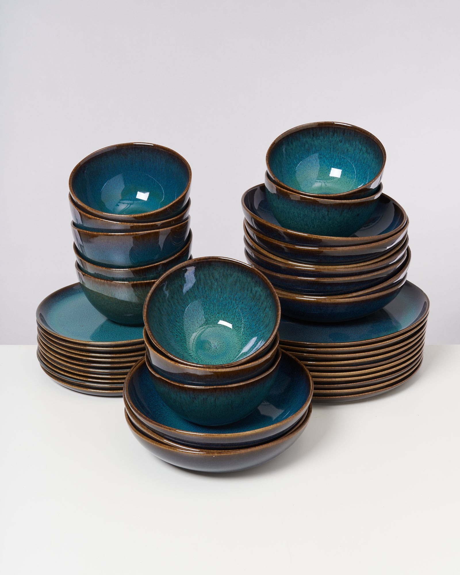 Ein Stapel von blau-grünen Keramikschalen und Tellern auf weißem Hintergrund.