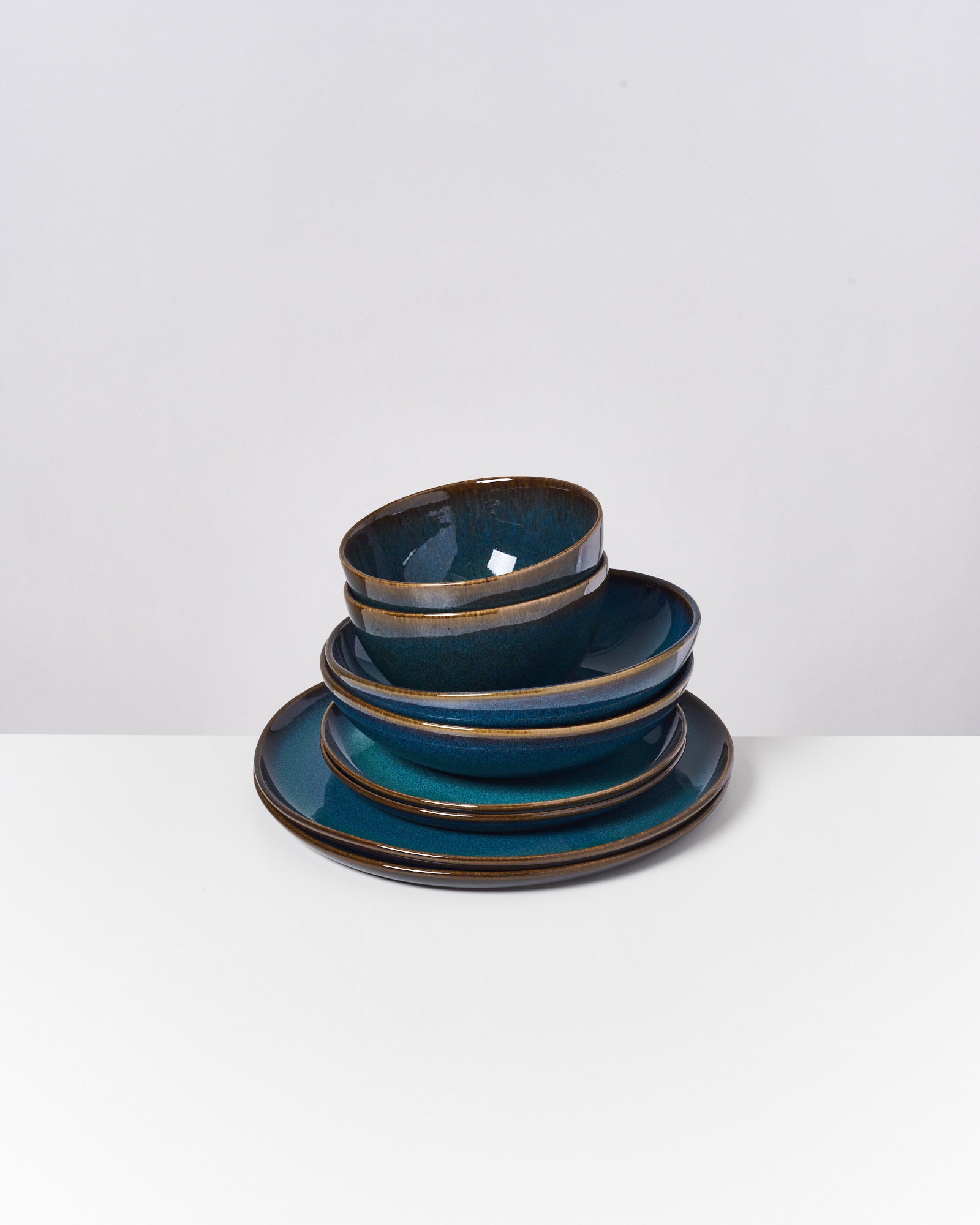 Ein Stapel aus sechs blauen Schalen und Tellern mit braunem Rand auf einem weißen Hintergrund.