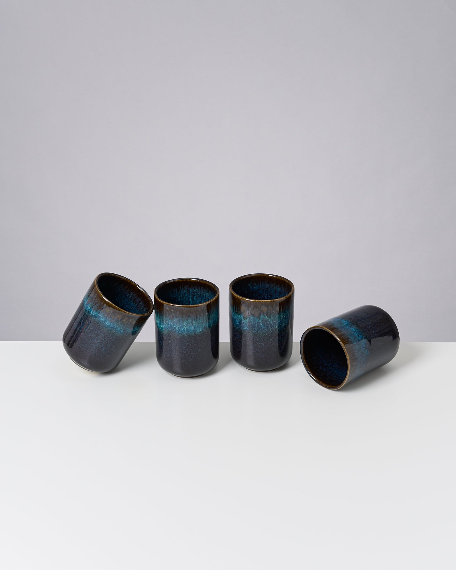 Vier dunkelblaue Keramiktassen stehen auf einem weißen Tisch, eine liegt auf der Seite.