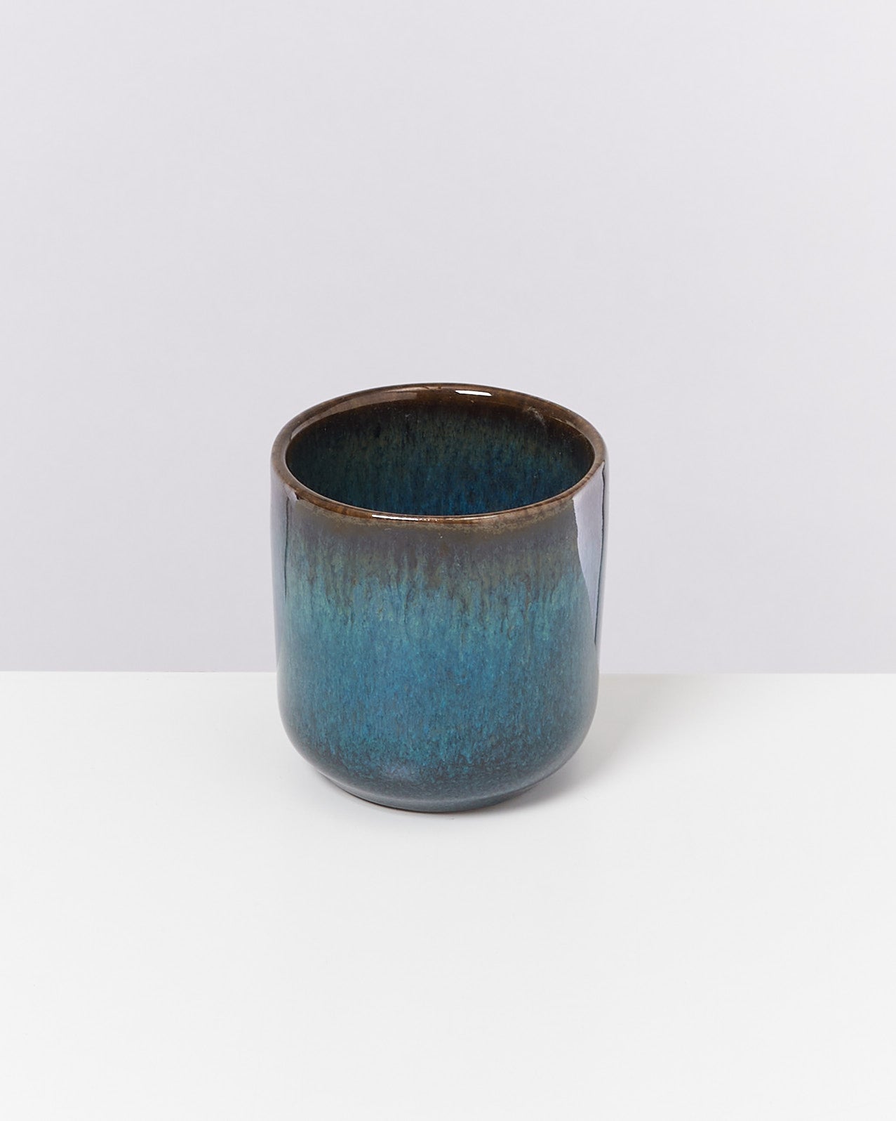 Keramikbecher mit blau-brauner Glasur auf weißem Hintergrund.