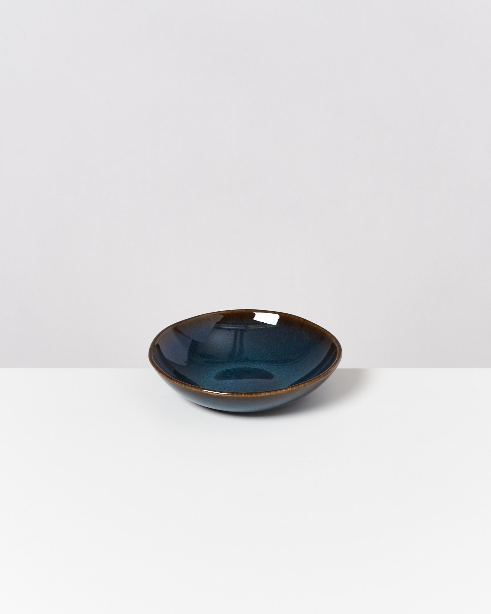 Eine kleine, runde, dunkelblaue Schale steht auf einer weißen Oberfläche vor einem grauen Hintergrund.