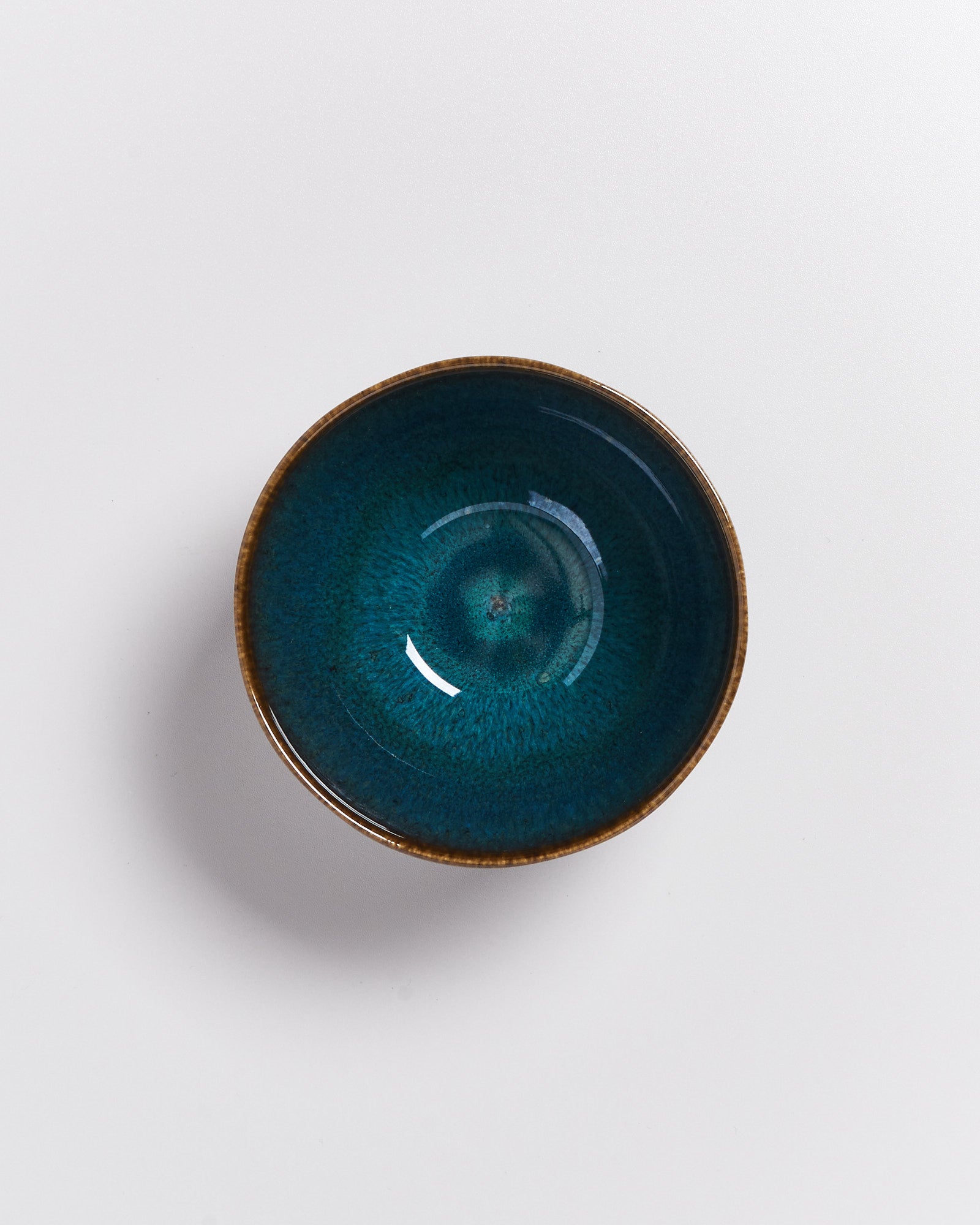 Keramikschüssel mit blaugrünem Inneren und braunem Rand auf weißem Hintergrund.